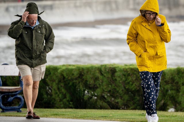 <p>People pull down their hoods to shelter from the wind as they walk along the sea front in Porthcawl, Wales</p>