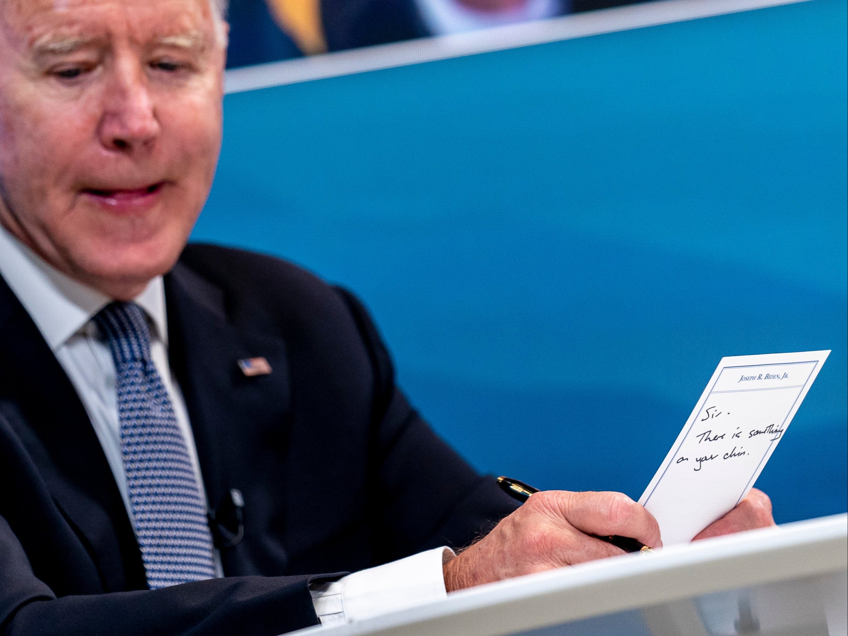 President Joe Biden holds a card handed to him by an aide that reads "Sir, there is something on your chin"