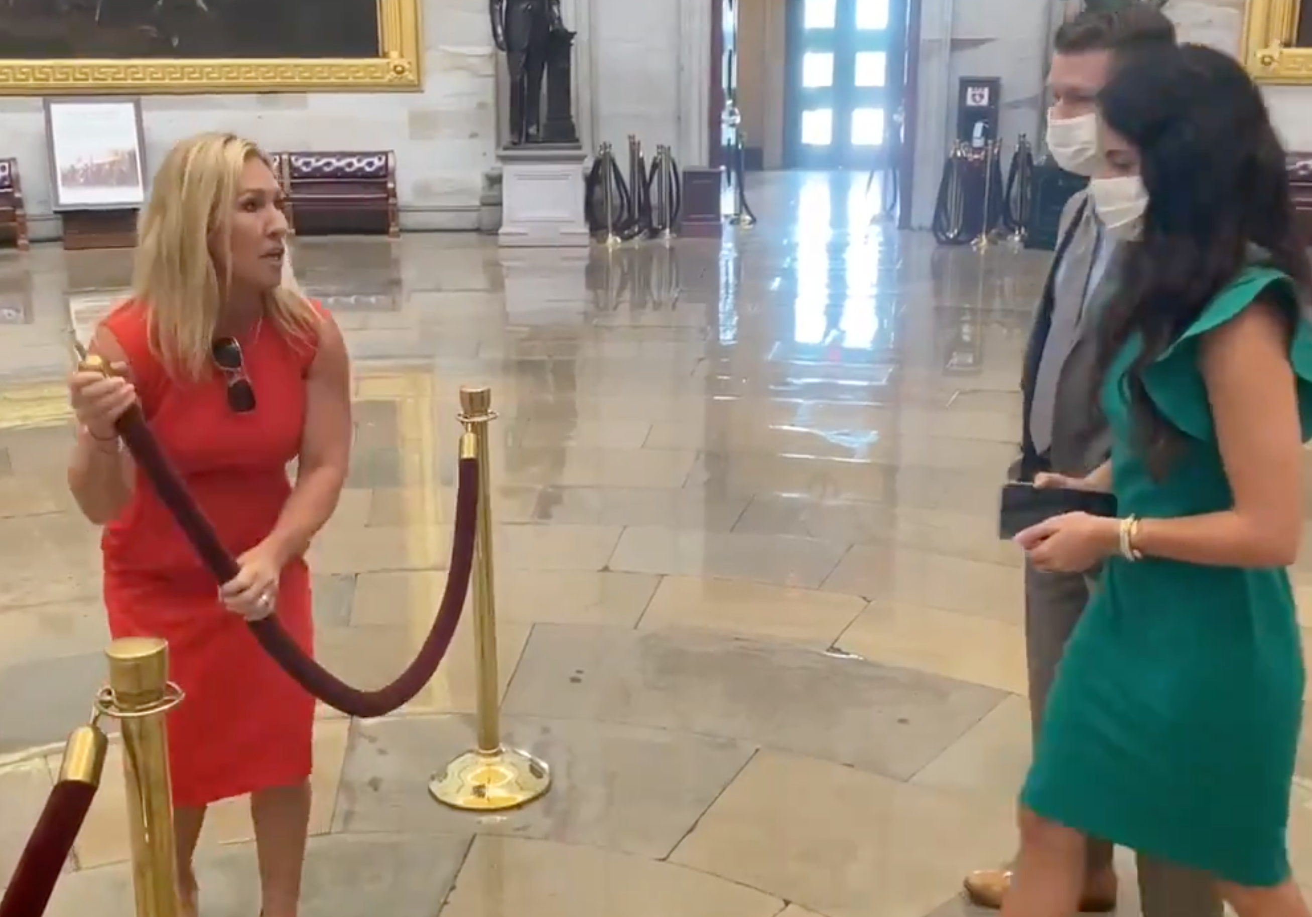 <p>Marjorie Taylor Greene ushers two unidentified people through her “Covid checkpoint Charlie"</p>