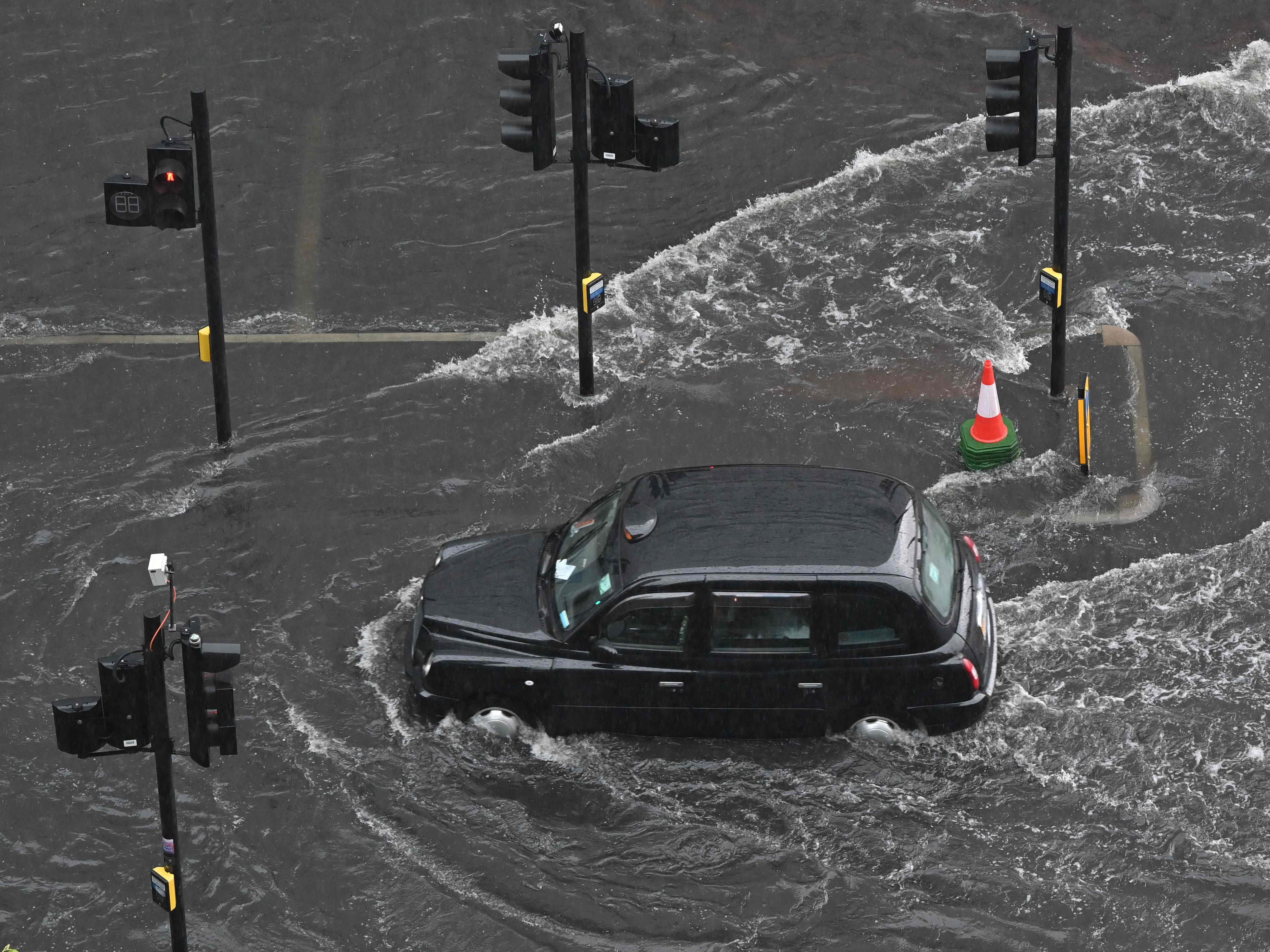A London taxi drives through water during flash floods in July