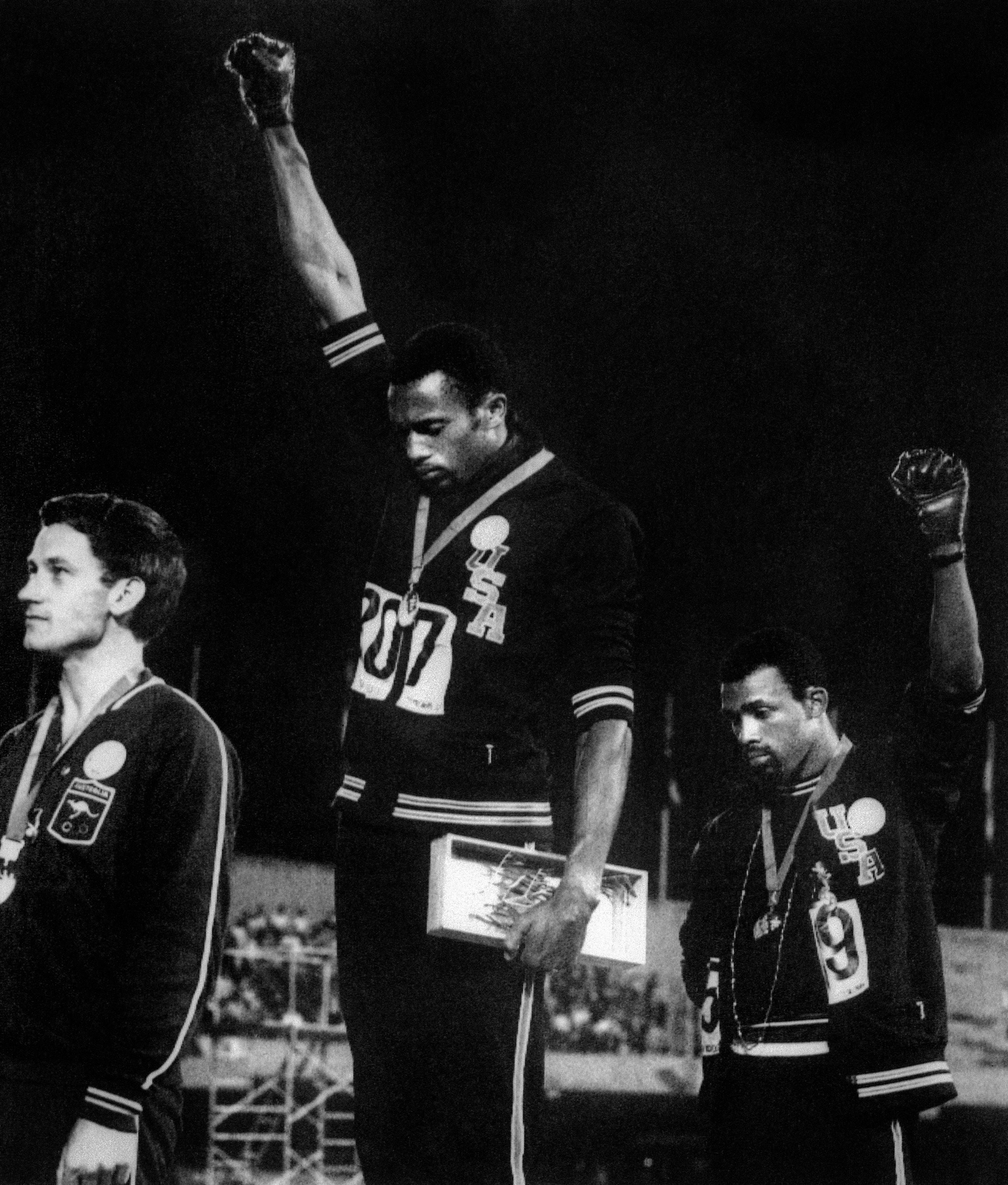 US athletes Tommie Smith (C) and John Carlos (R) raise their gloved fists in the Black Power salute to express their opposition to racism in the USA during the national anthem