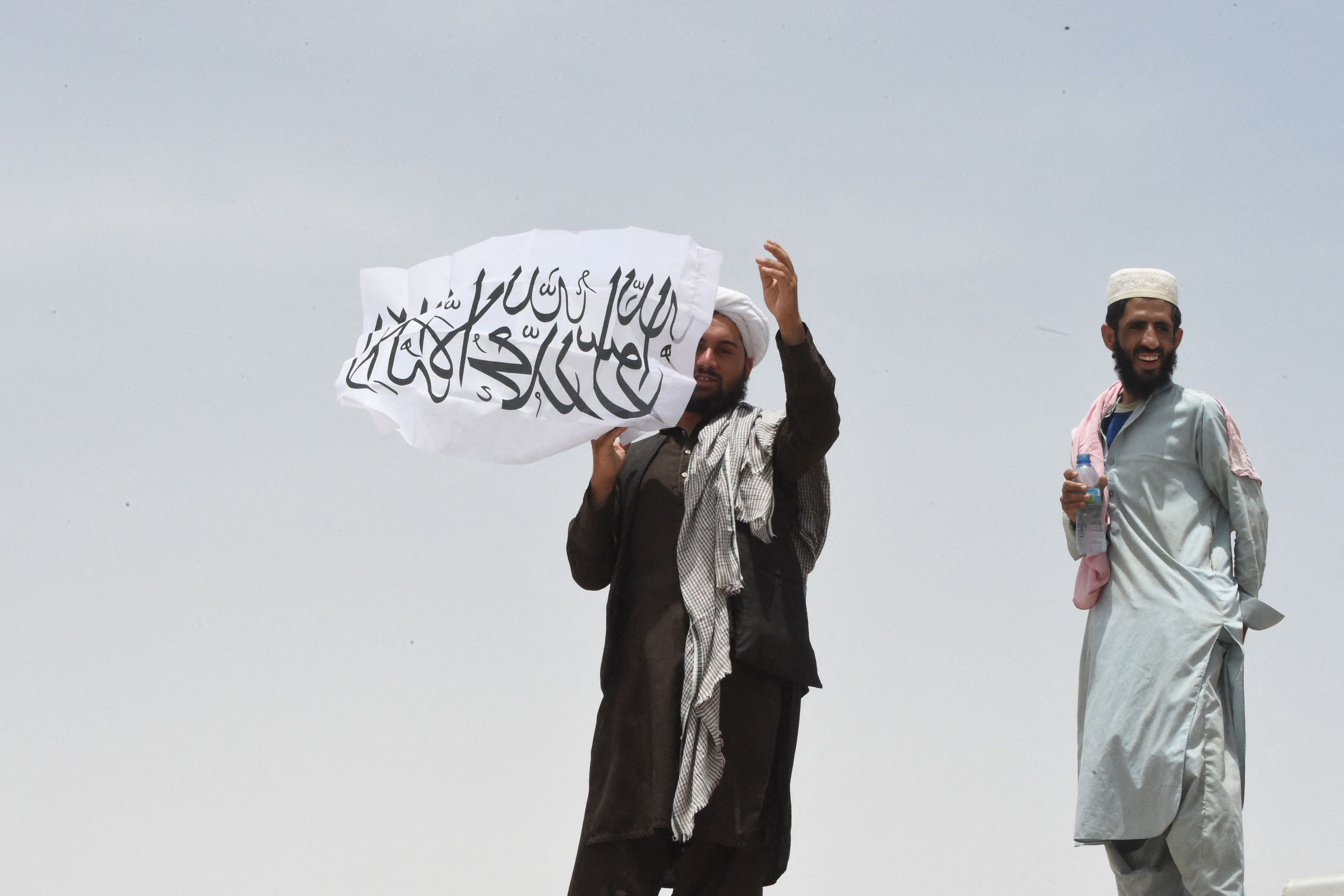 A man standing on the Afghan side of the border holds a Taliban flag near a crossing point in Pakistan