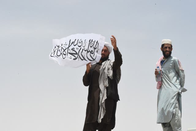 <p> A man standing on the Afghan side of the border holds a Taliban flag near a crossing point in Pakistan</p>