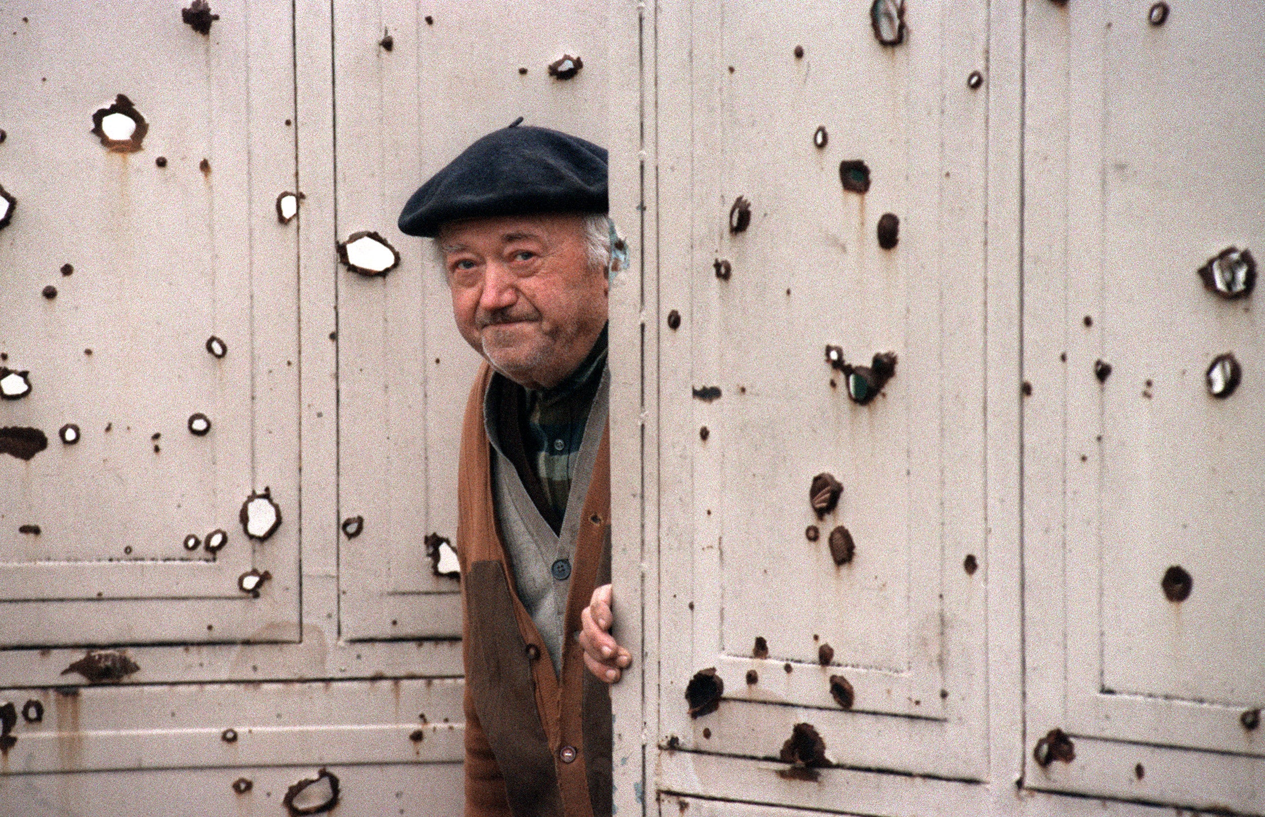 An elderly inhabitant timidly looks around the bullet-ridden door to his house in Vukovar, 29 November 1991