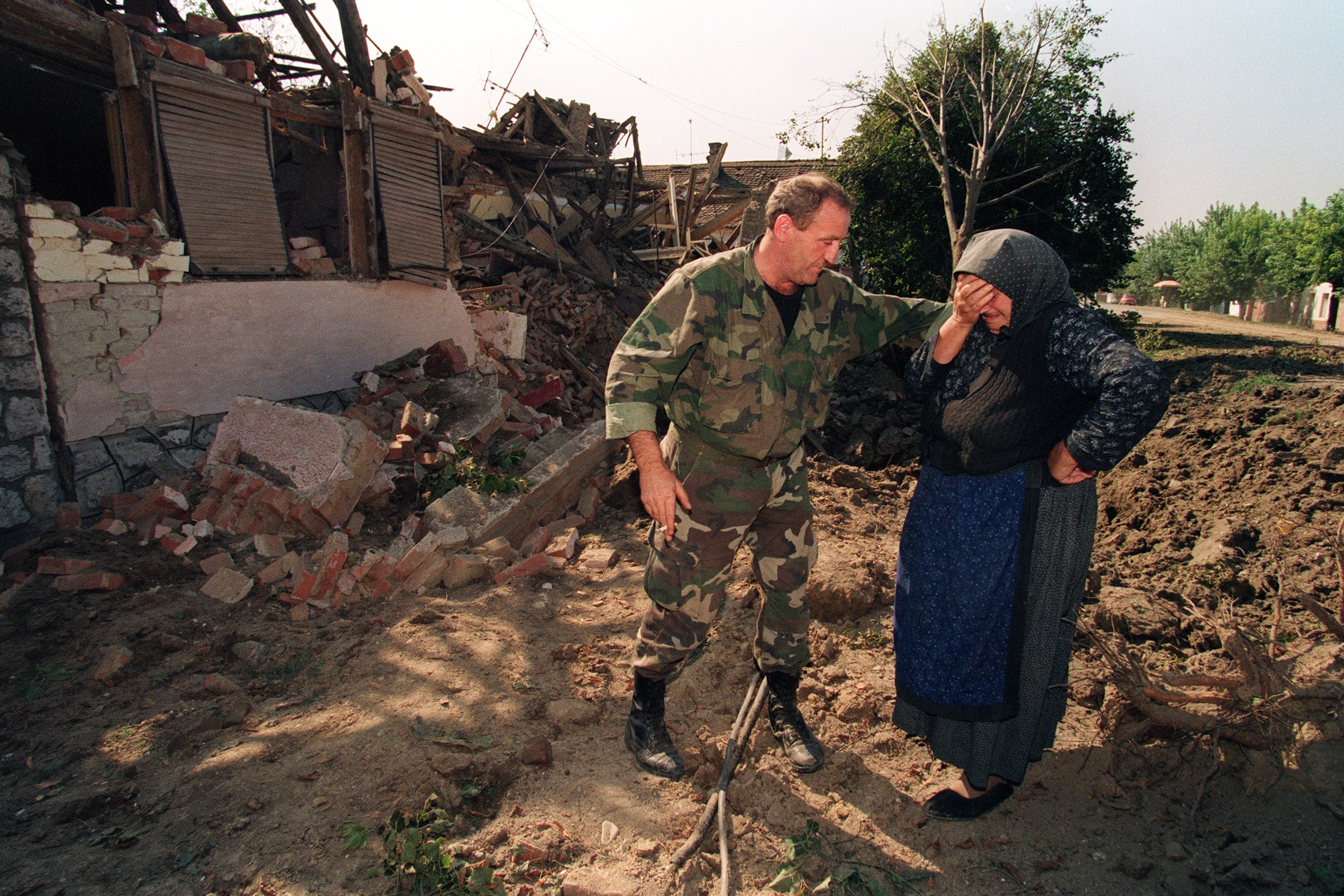 A Croatian national guardsman comforts an old woman outside her home which was destroyed in an air raid during the night by Serbian air forces, 26 September 1991