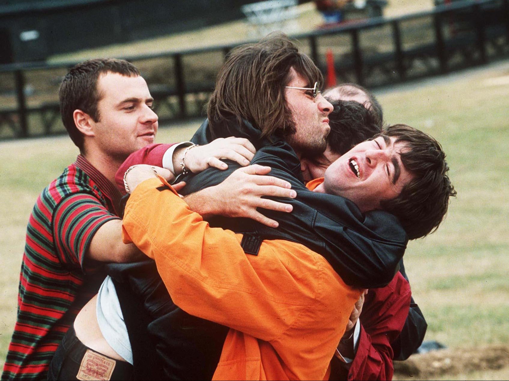 Alan White, Liam Gallagher, Noel Gallagher in a group hug with fellow Oasis members Paul ‘Guigsy’ McGuigan and Paul ‘Bonehead’ Arthurs before their show at Knebworth, 1996