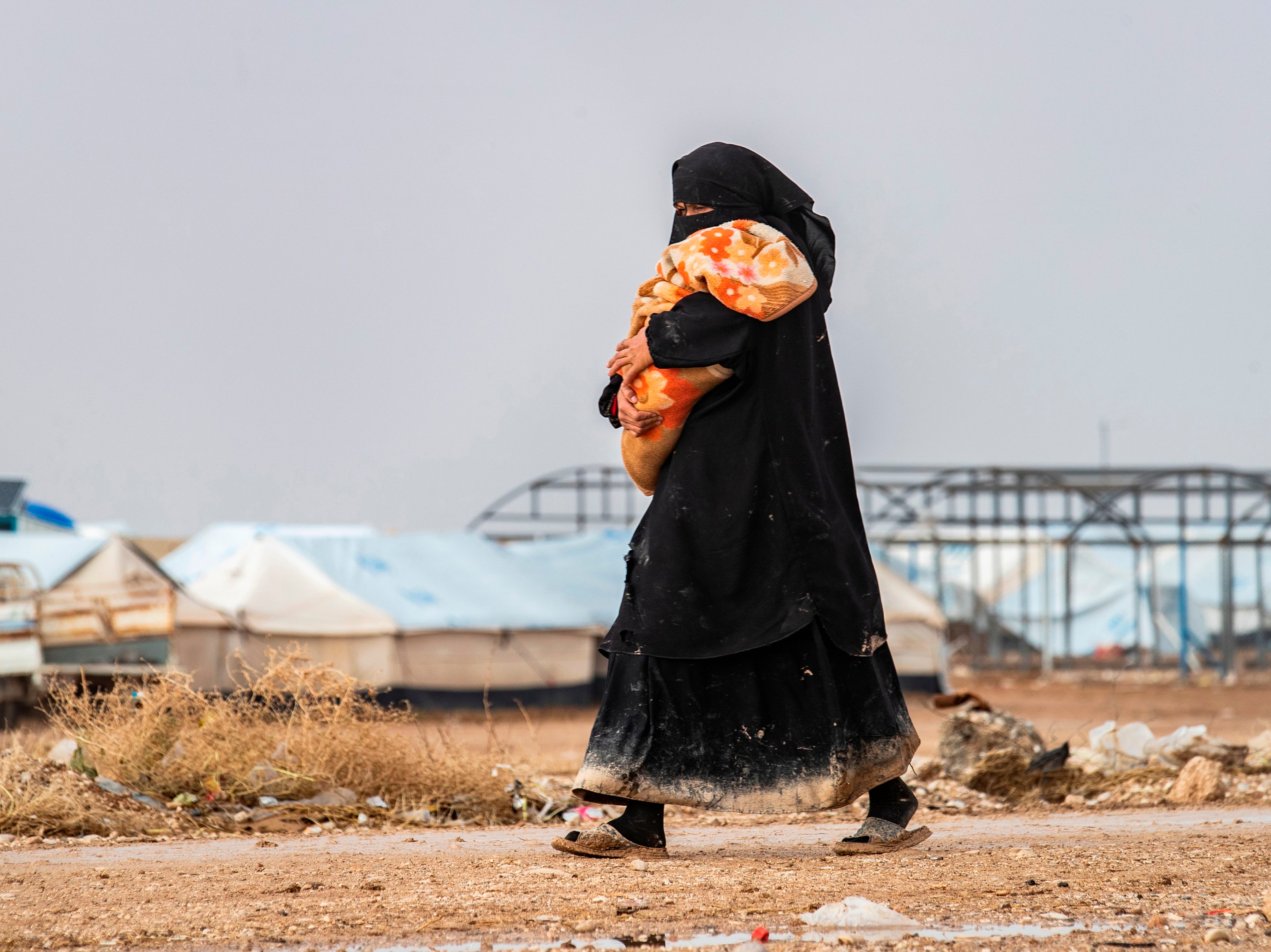 A woman carrying a toddler walks at the Kurdish-run al-Hol camp for the displaced where families of Islamic State (IS) foreign fighters are held, in the al-Hasakeh governorate in northeastern Syria on 9 December 2019