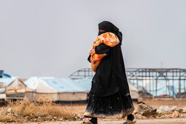 <p>A woman carrying a toddler walks at the Kurdish-run al-Hol camp for the displaced where families of Islamic State (IS) foreign fighters are held, in the al-Hasakeh governorate in northeastern Syria on 9 December 2019</p>