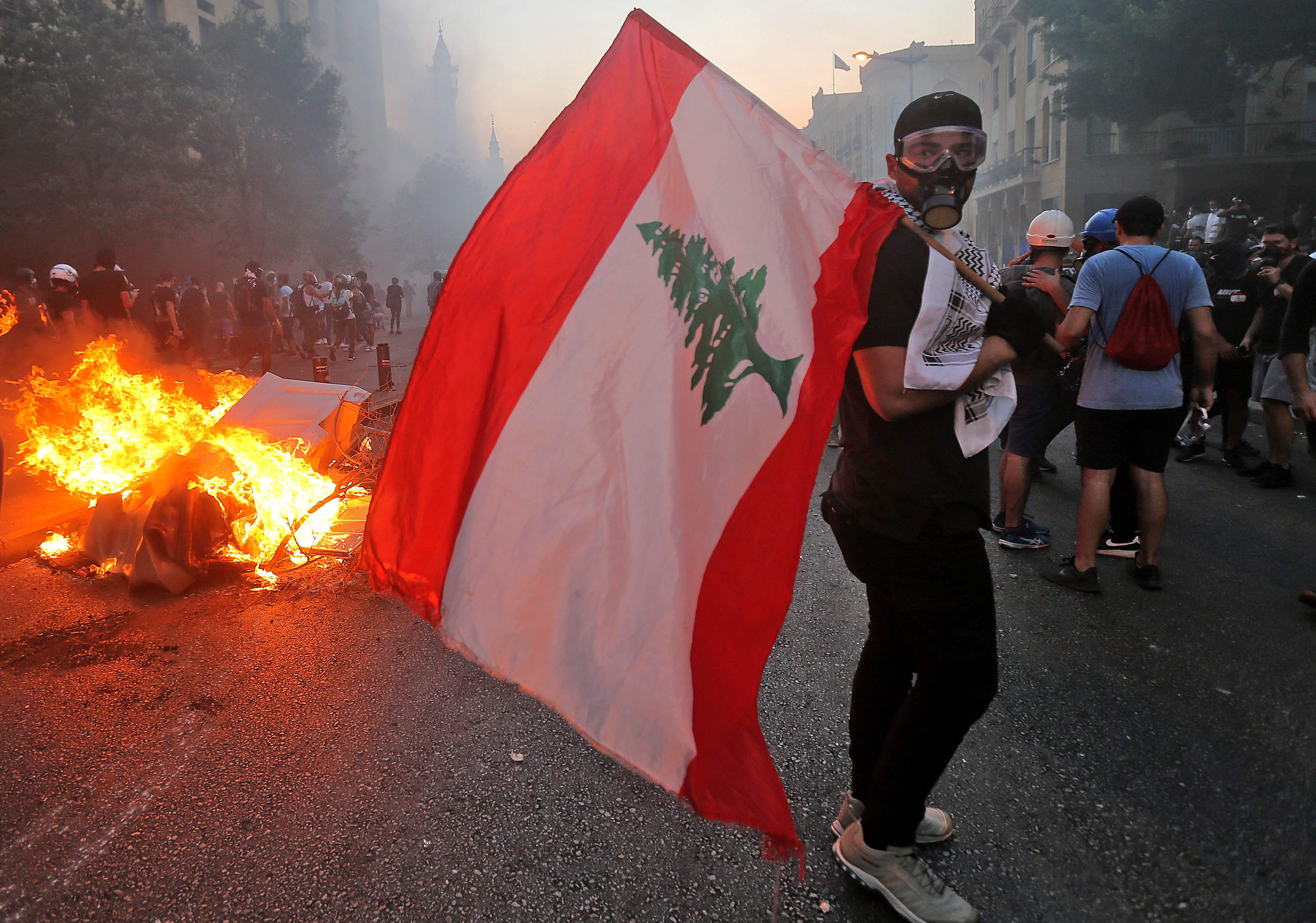 A protester stands with a Lebanese national flag during clashes with army and security forces near the Lebanese parliament