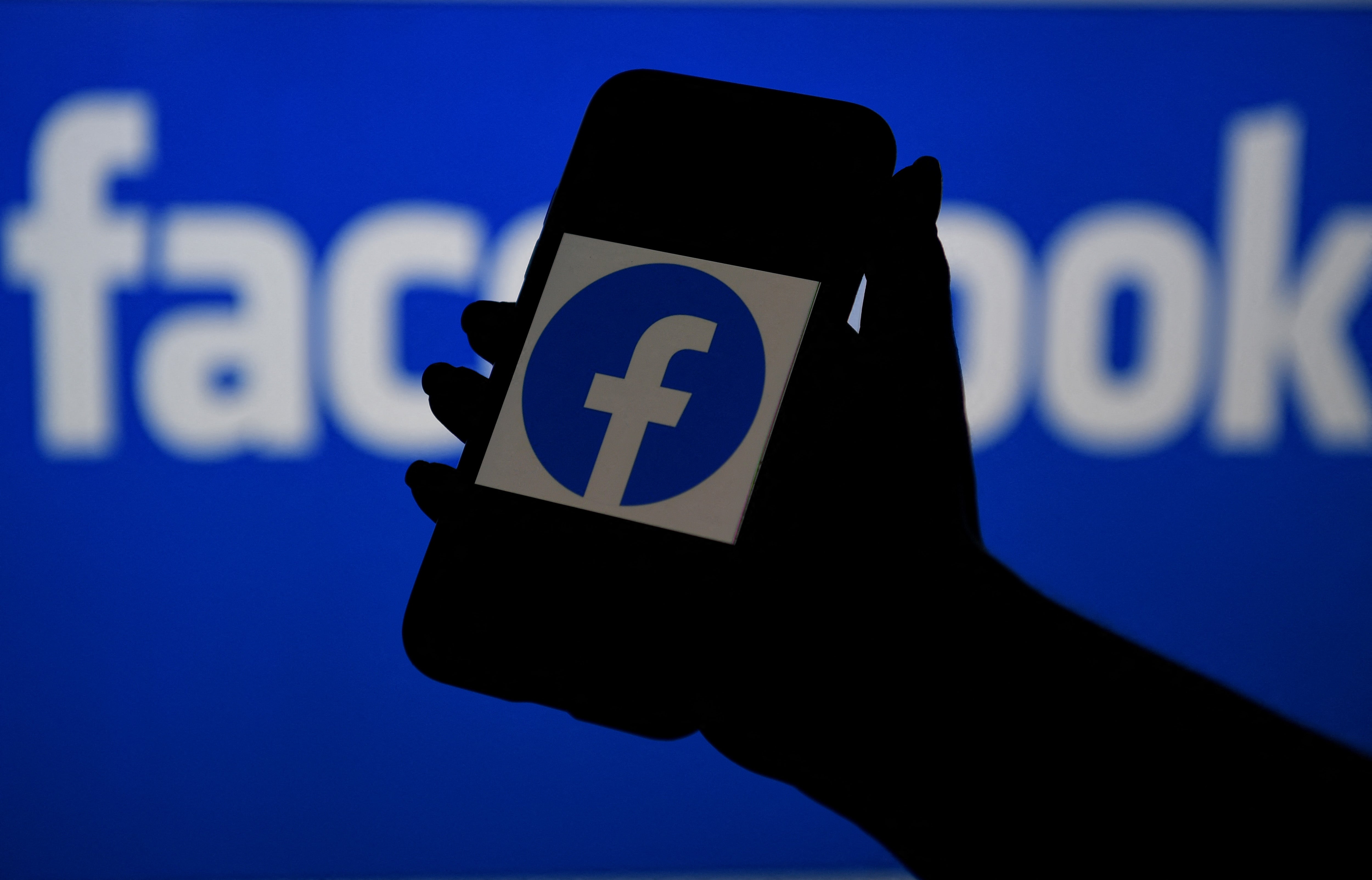 <p>Smart phone screen displays the logo of Facebook on a Facebook website background</p>