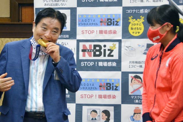 <p>Nagoya city Mayor Takashi Kawamura bites the Tokyo 2020 Olympic Games gold medal of the softball athlete Miu Goto during a ceremony in Nagoya, central Japan, 4 August 2021</p>
