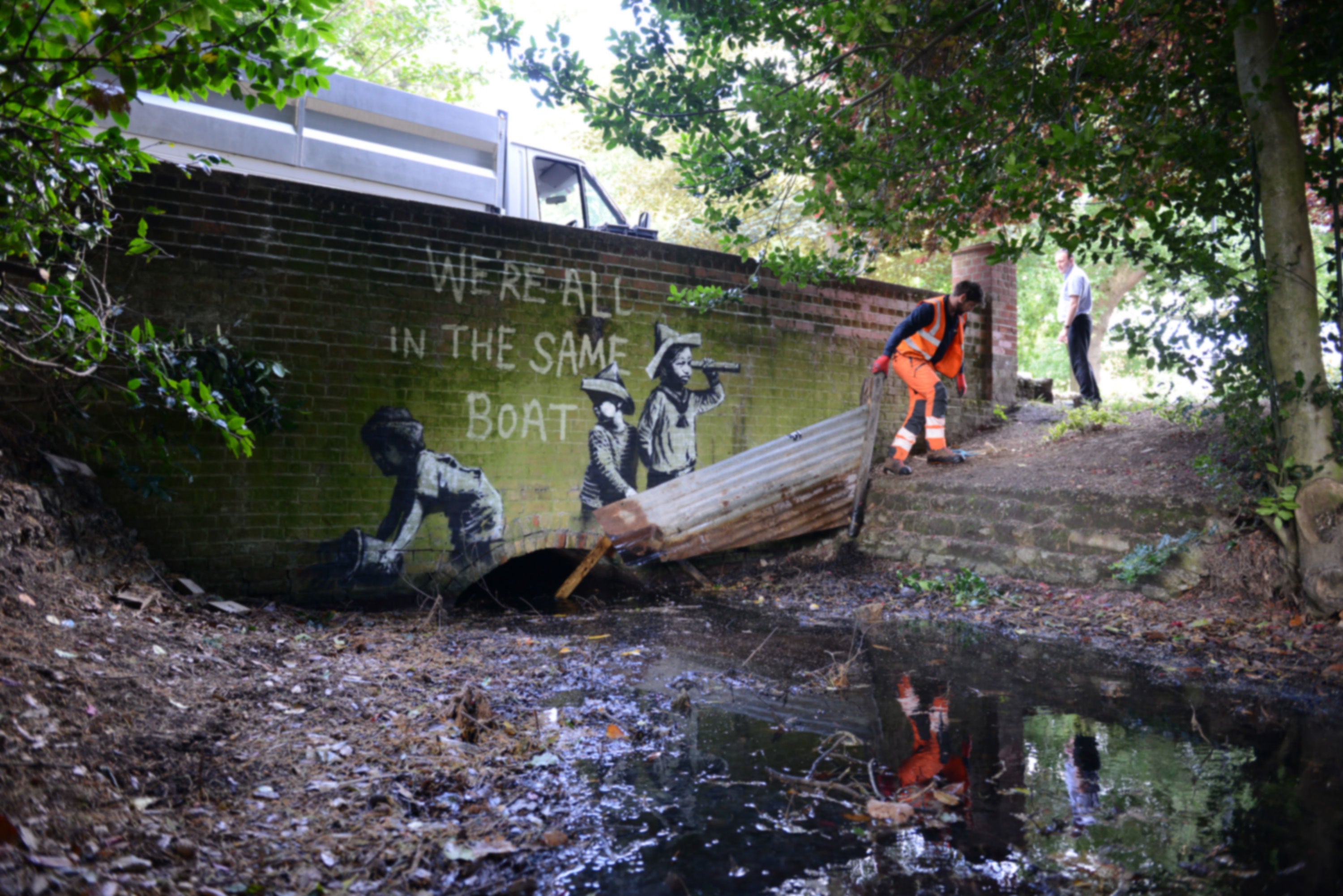 A man in orange overalls removes part of a piece of street art which has appeared on a wall in Nicholas Everitt Park, Lowestoft, Suffolk, which is believed to be a new work by street artist Banksy.