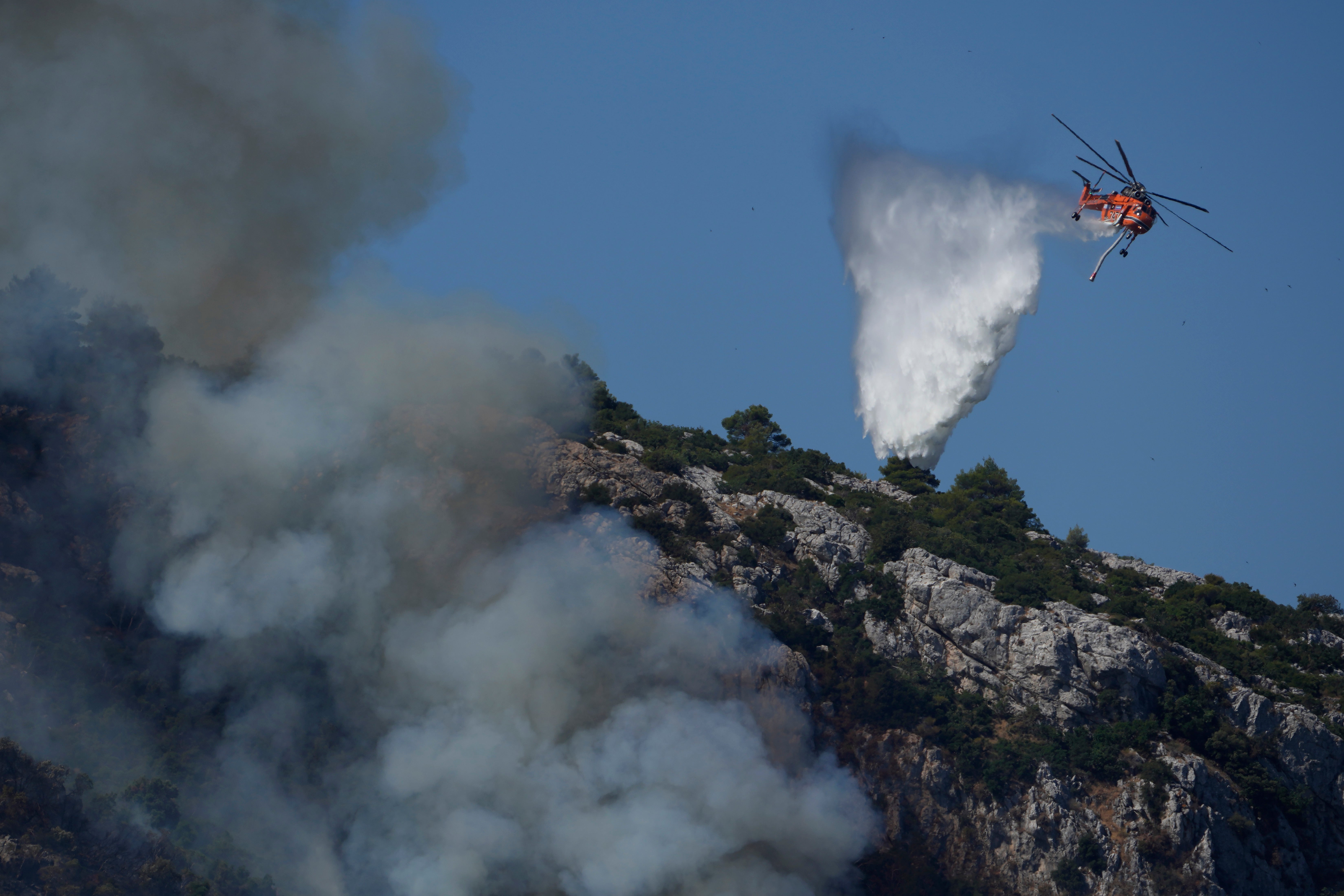 A helicopter drops water on a fire near Malakasa in northern Athens