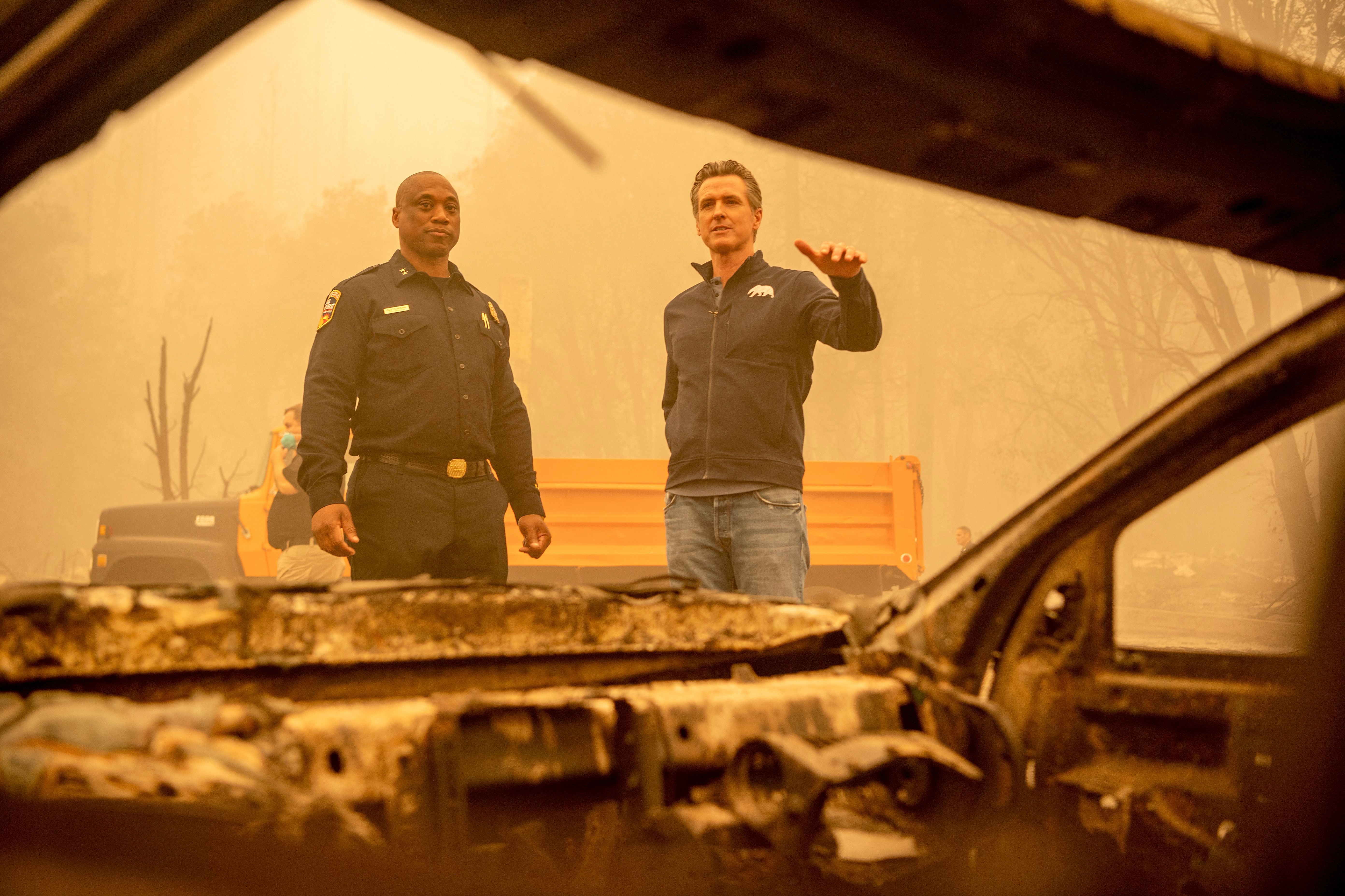 California Governor Gavin Newsom (R) looks at a burned vehicle alongside Assistant Region Chief for Cal Fire Curtis Brown (L) in downtown Greenville on Saturday