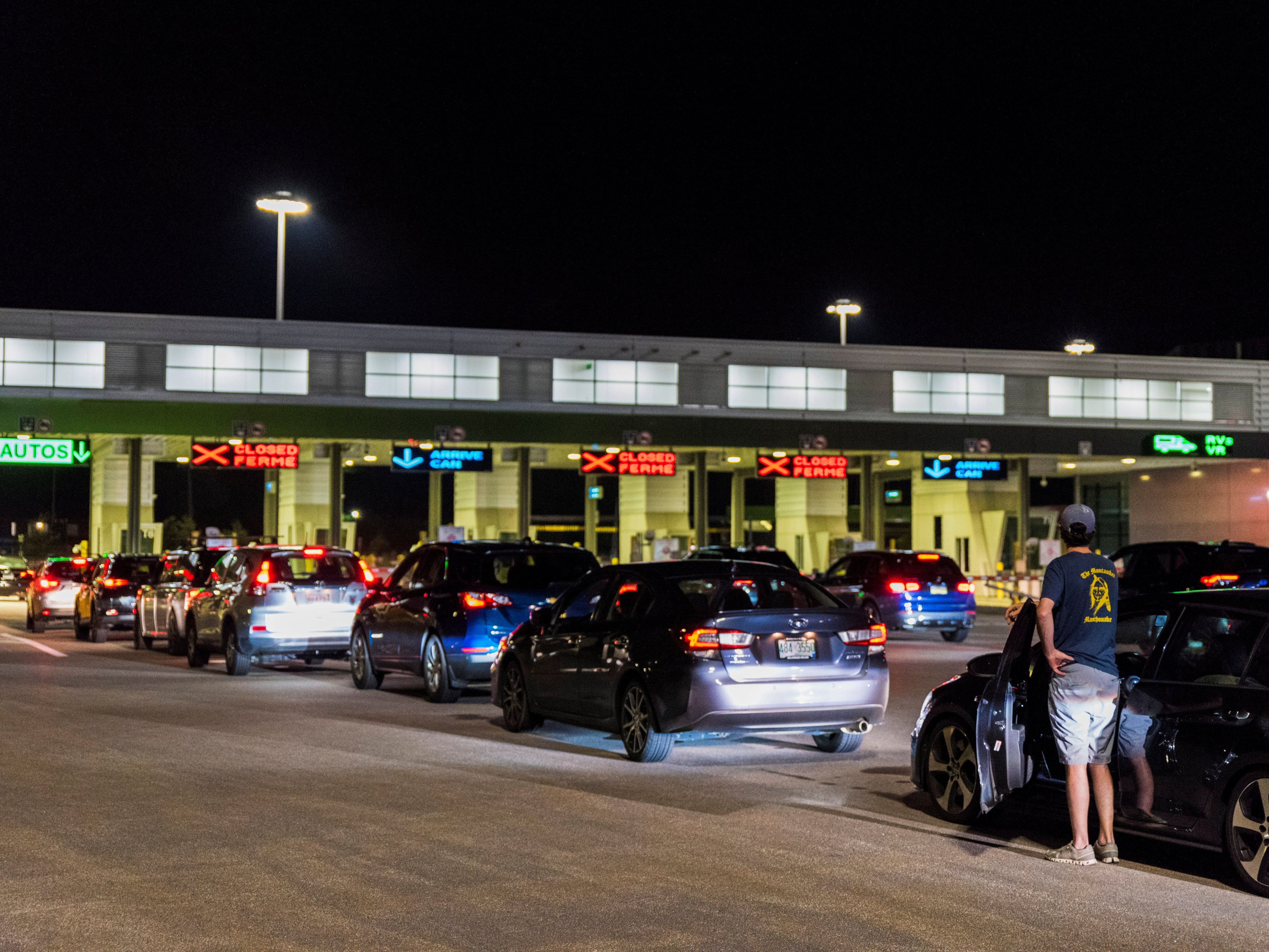 <p>A man peers out over his car door at the line of travellers waiting to enter Canada</p>