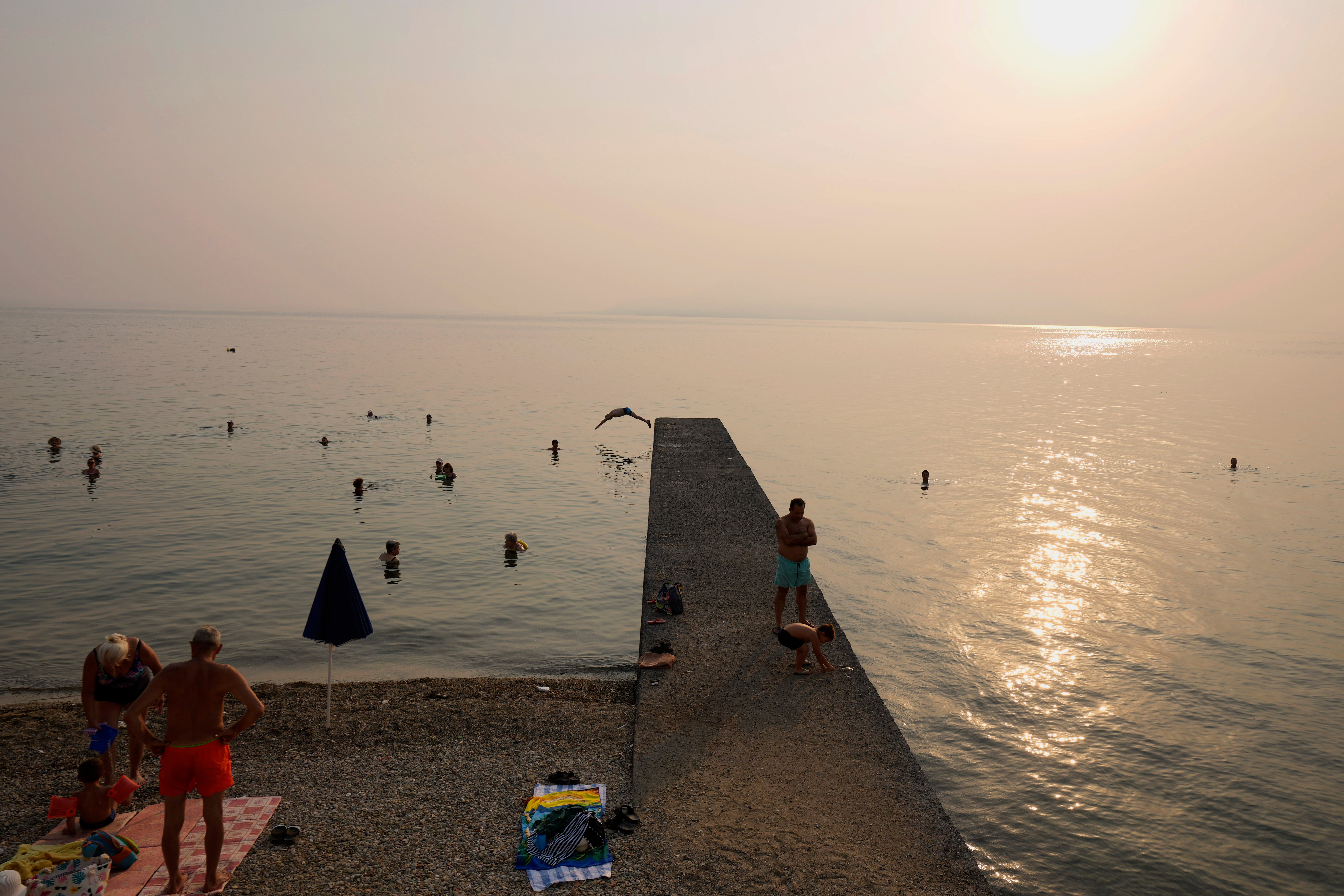 Smoke from the wildfires spreads over people as they enjoy the sea at Edipsos on Evia island