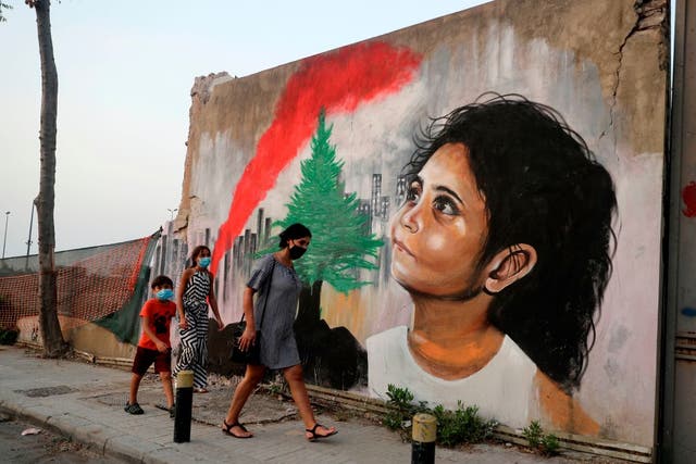 <p>Mask-wearing pedestrians walk past a mural depicting a young Lebanese girl who suffered a face injury in the 4 August blast in Beirut</p>