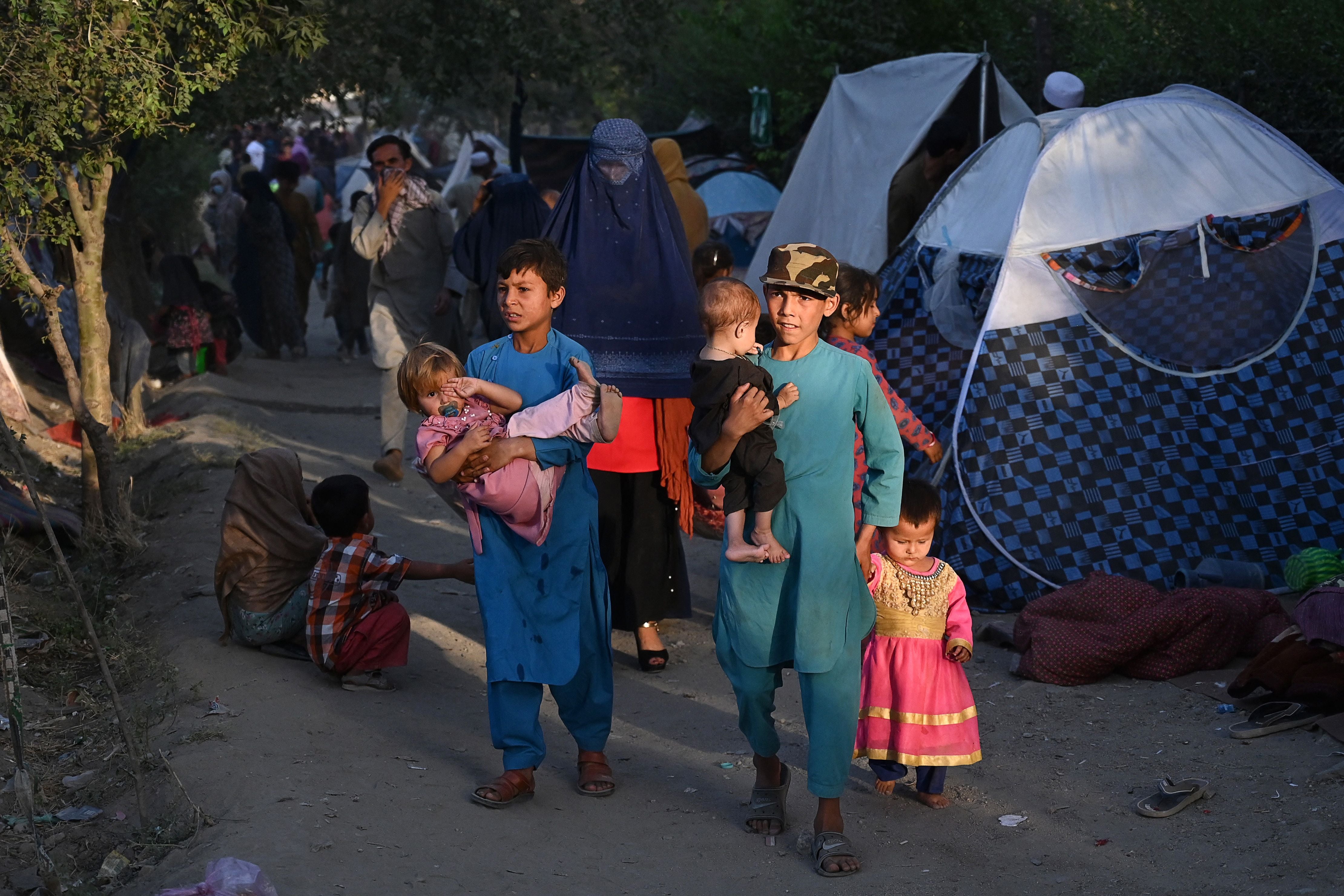 Internally displaced Afghan families, who fled from Kunduz, Takhar and Baghlan province due to battles between Taliban and Afghan security forces, walk past their temporary tents at Sara-e-Shamali in Kabul on 11 August, 2021. - A former US ambassador to Afghanistan has said that Joe Biden is abandoning the country in its hour of need.