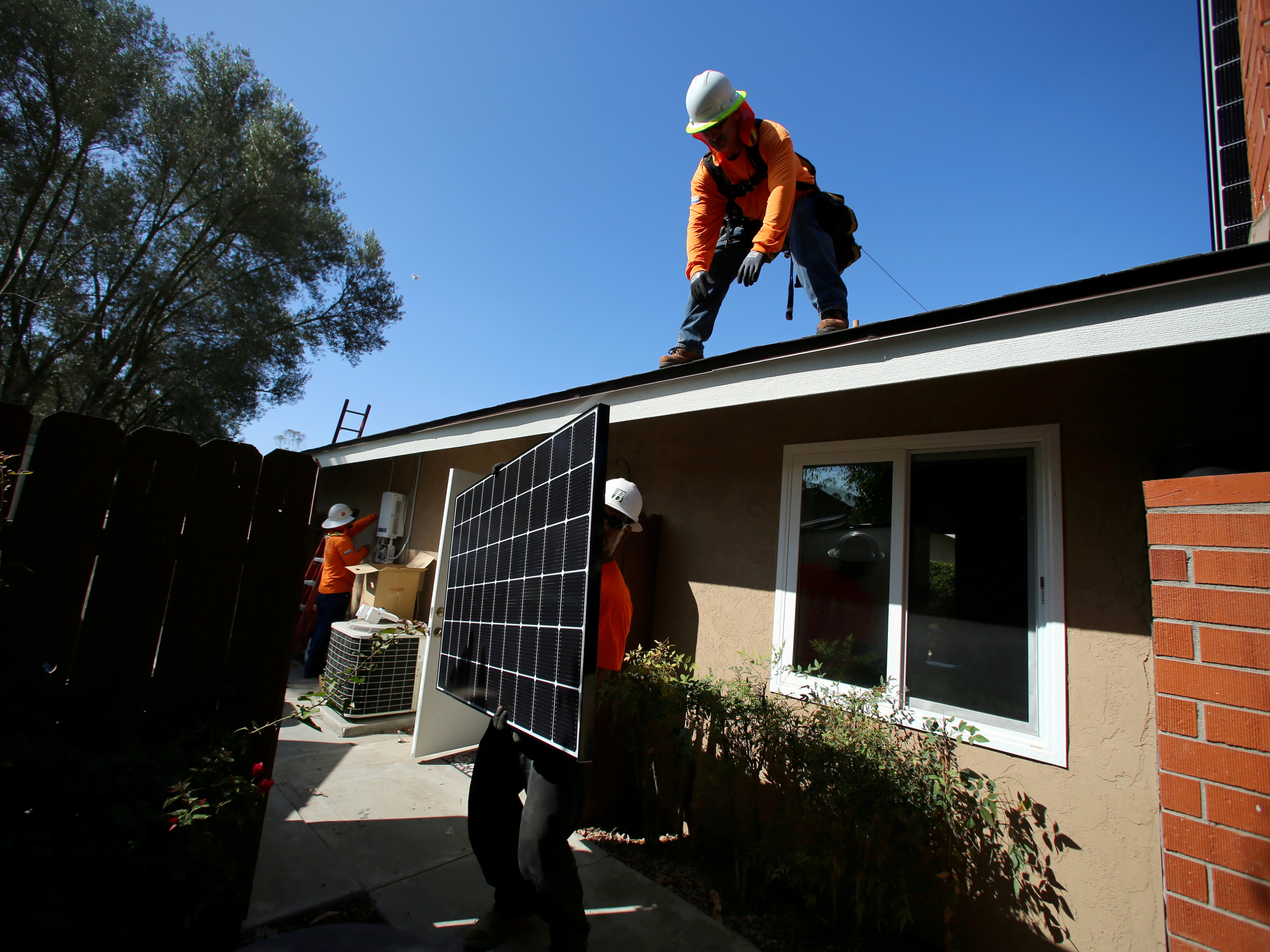 <p>Workers lift a solar panel onto a roof during a residential solar installation in Scripps Ranch, San Diego, California, US 14 October 2016</p>