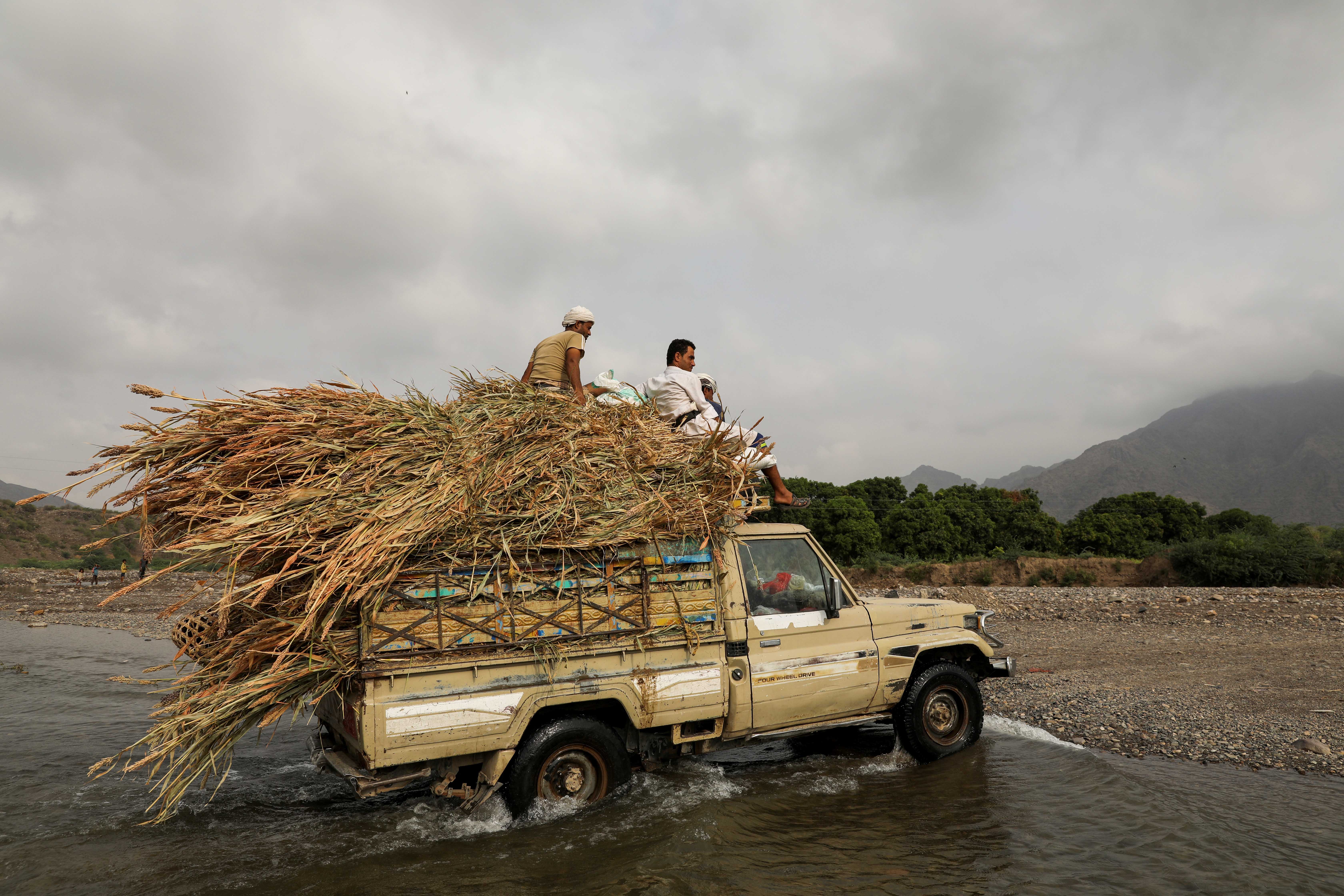 Villagers ride on top of a vehicle loaded with fodder as they cross a spring lake in the Khamis Banisaad district