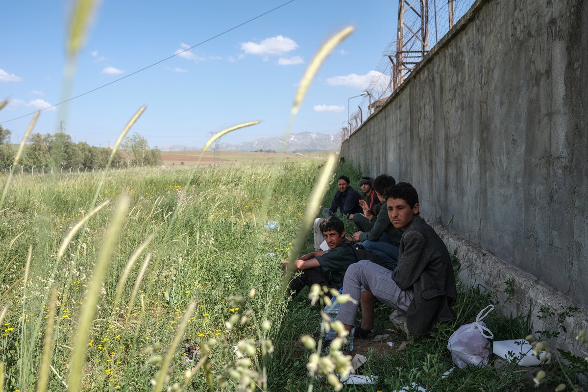 Afghans and Iranians rest near a former oil refinery wall, where they will likely to be waiting three days