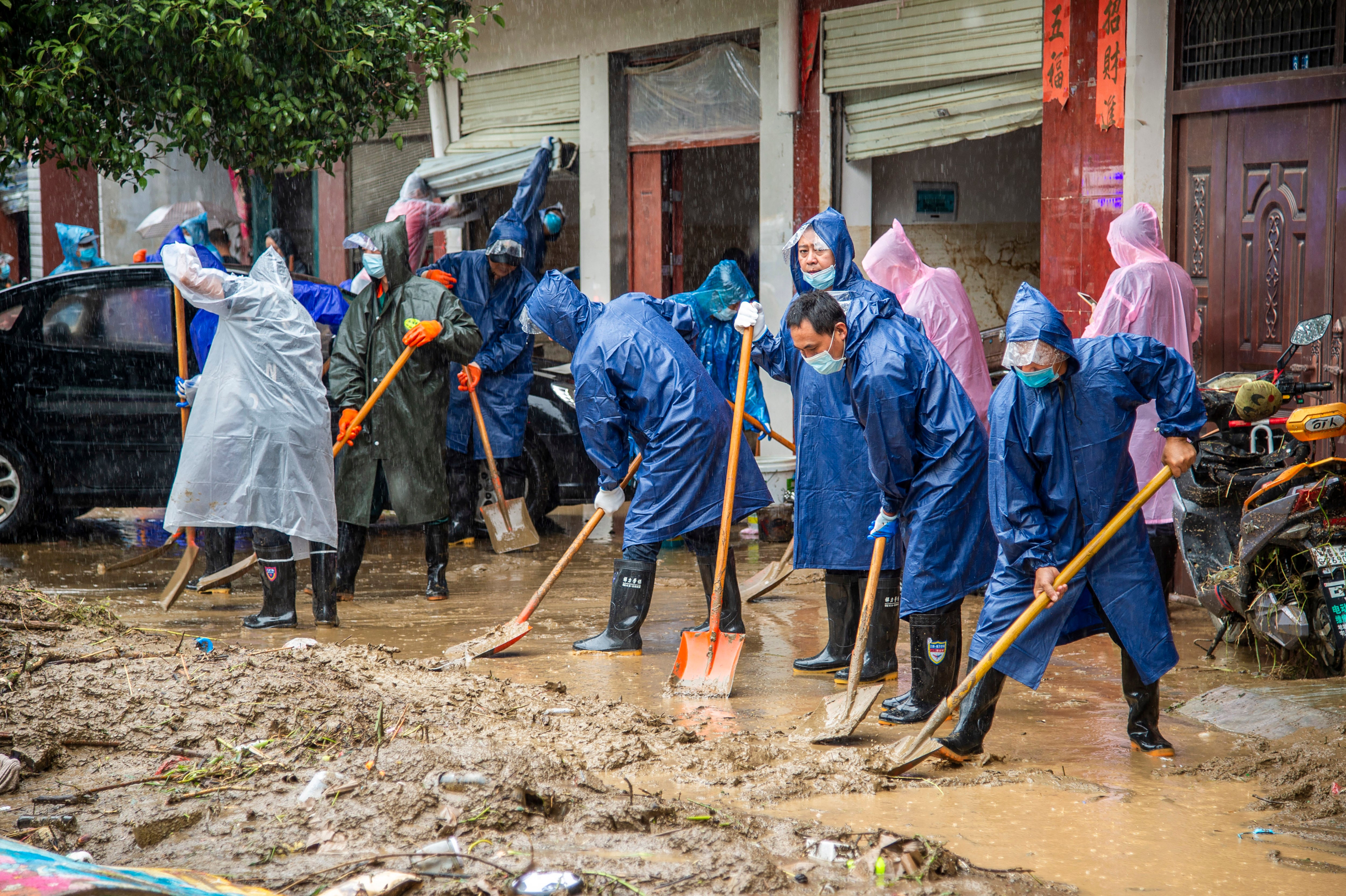 People shovel debris and mud from a road in Liulin Township of Suixian County in central China's Hubei Province as flooding in central China continued to cause havoc in both cities and rural areas, with authorities saying Friday that more than 20 people had been killed and another several were missing