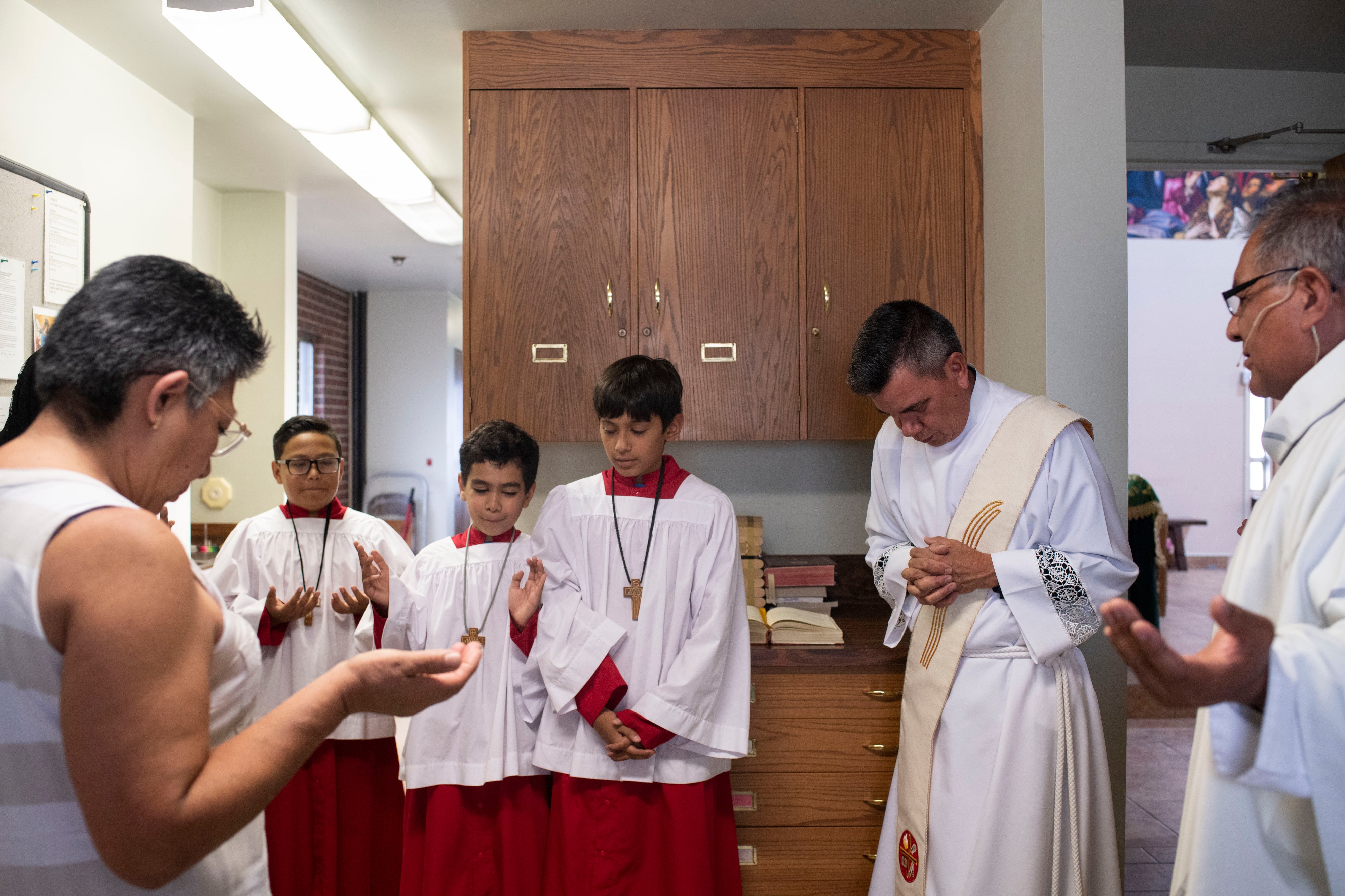 From center left, Diego Sanchez, 11, Jordan Vielma, 9, and Estevan Vielma, 11, stand with Deacon Mario Vielma and Pastor Jorge de los Santos in prayer before Mass at Our Lady Mother of the Church in Commerce City, Colorado, on July 15