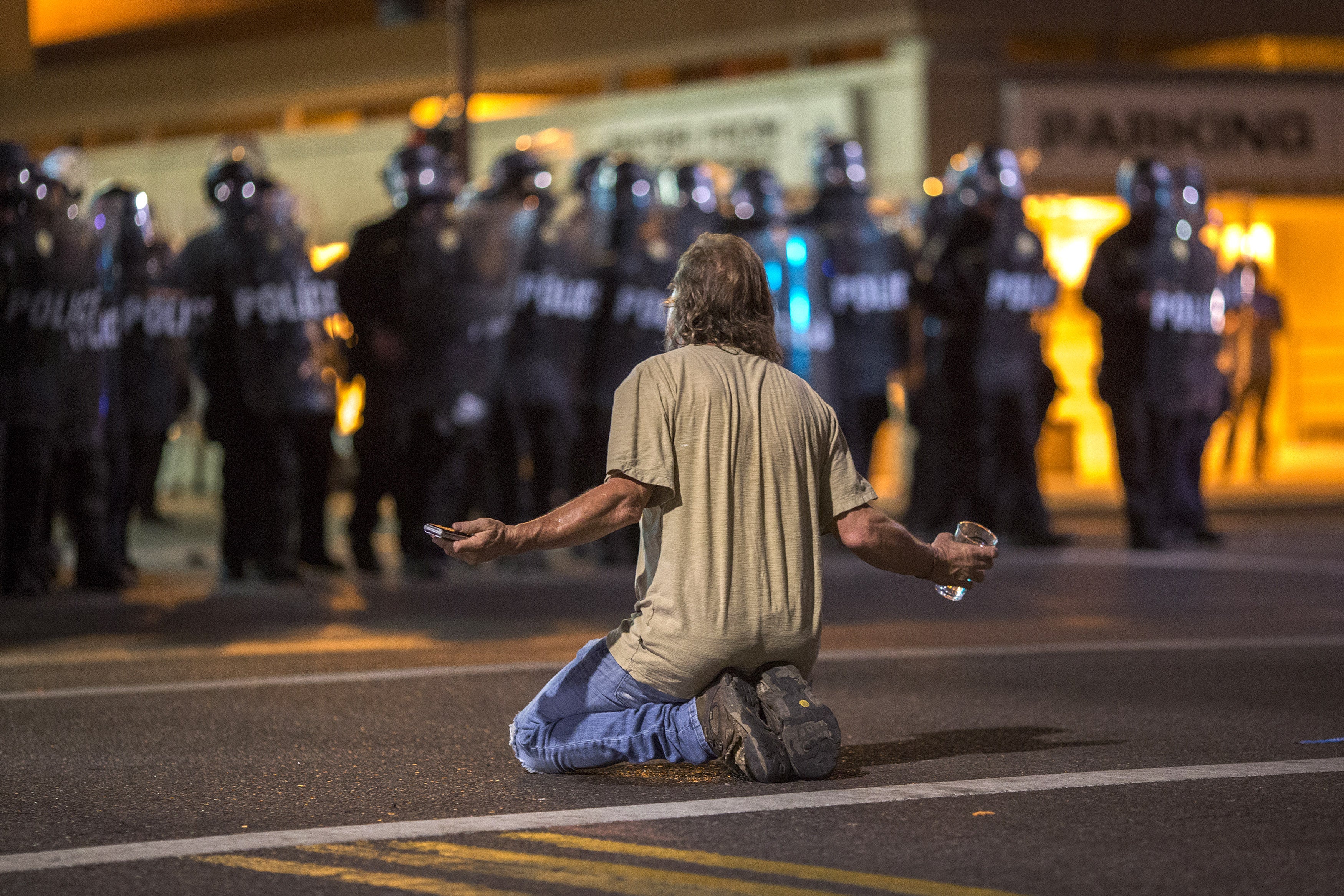 A man kneels in the street as police officers advance upon demonstrators after a rally by President Donald Trump at the Phoenix Convention Center on August 22, 2017 in Phoenix, Arizona.