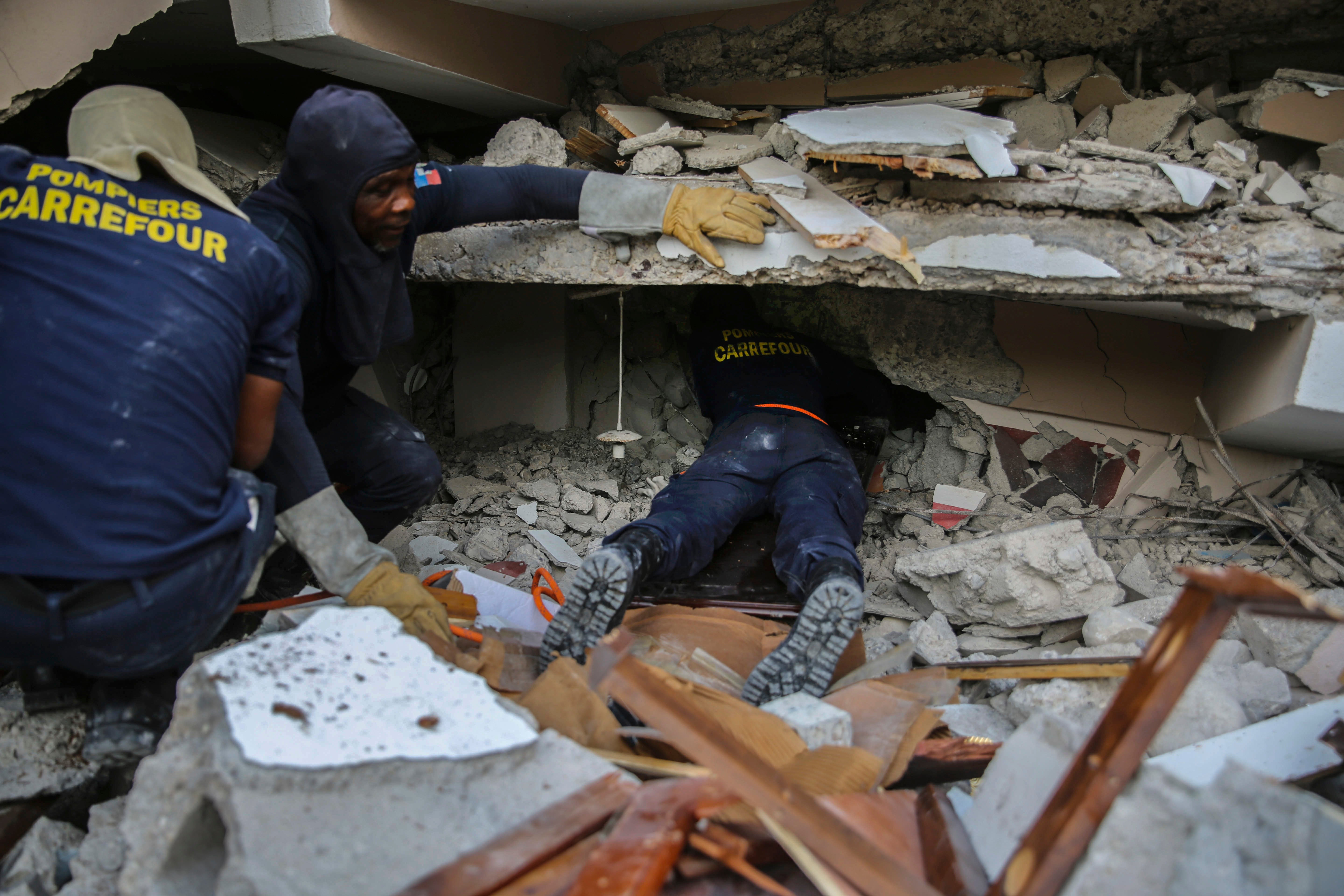 Firefighters search for survivors inside a collapsed building in the Haitian city of Les Cayes