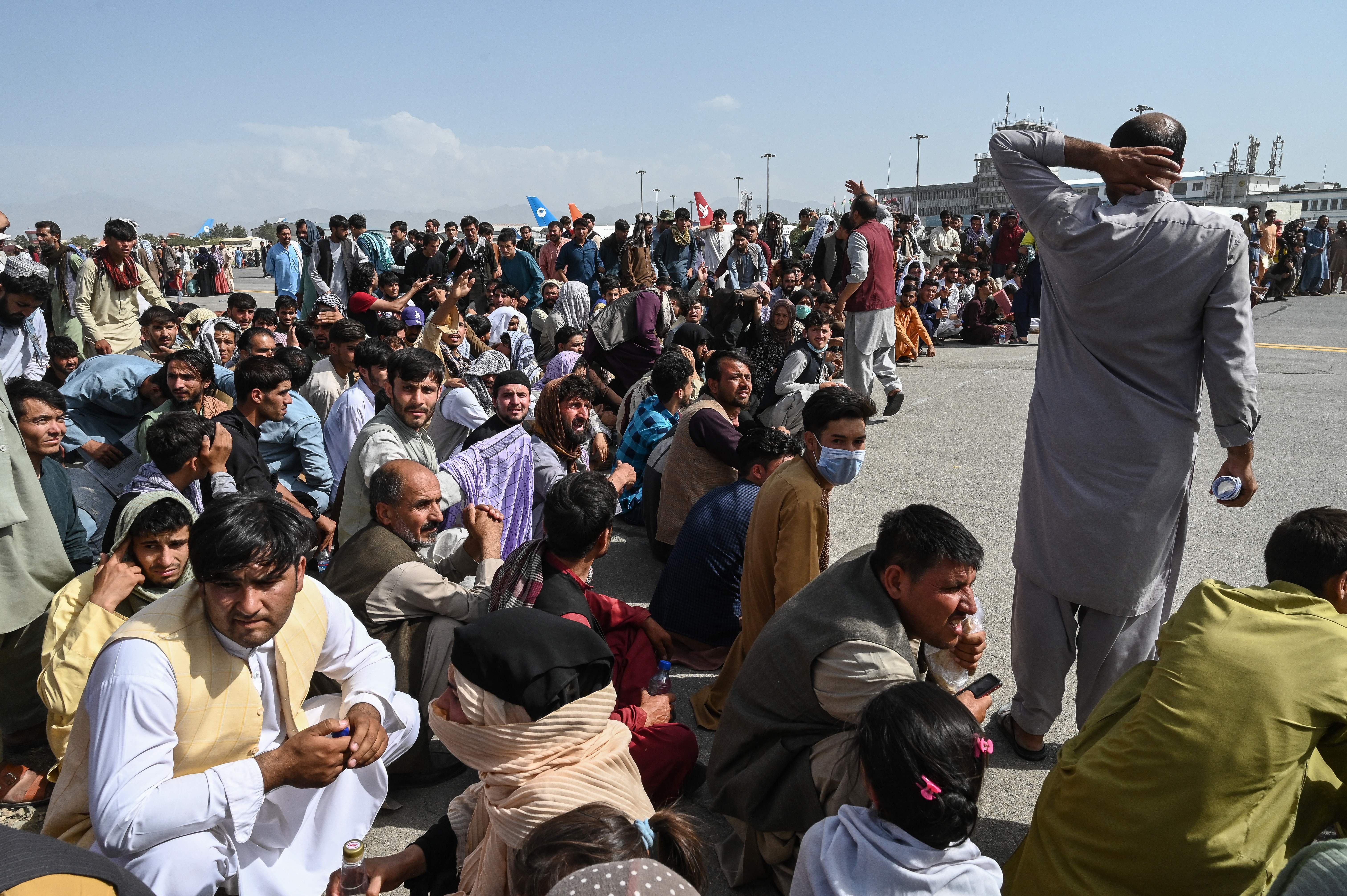 Escape route: Afghans sit on the tarmac at Kabul airport on Monday