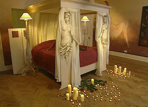 Two Greek nude sculptures carved out of MDF board flank a four-poster bed in a room makeover by Changing Rooms
