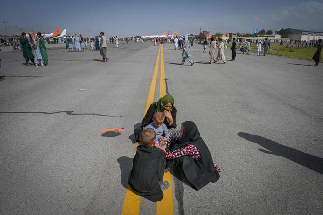 <p>Afghan people sit along the tarmac as they wait to leave the Kabul airport in Kabul on August 16, 2021, after a stunningly swift end to Afghanistan's 20-year war, as thousands of people mobbed the city's airport trying to flee the group's feared hardline brand of Islamist rule.</p>