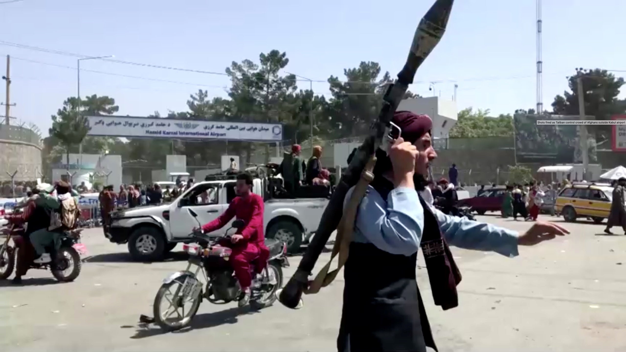 A Taliban fighter runs towards a crowd outside Kabul airport, Afghanistan