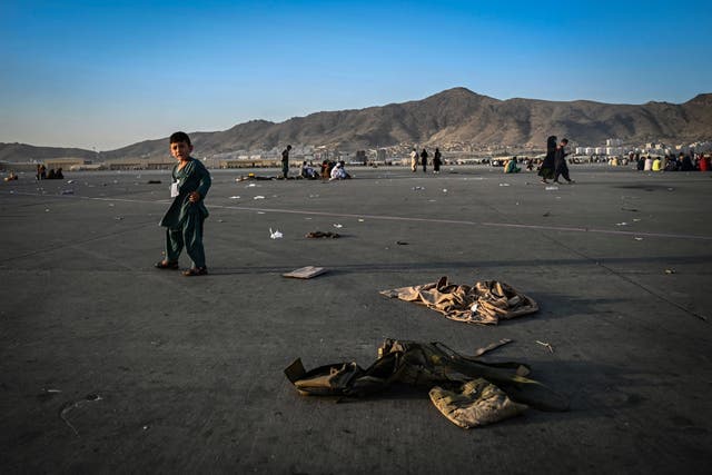 <p>An Afghan child walks near military uniforms as he with elders wait to leave the Kabul airport in Kabul</p>