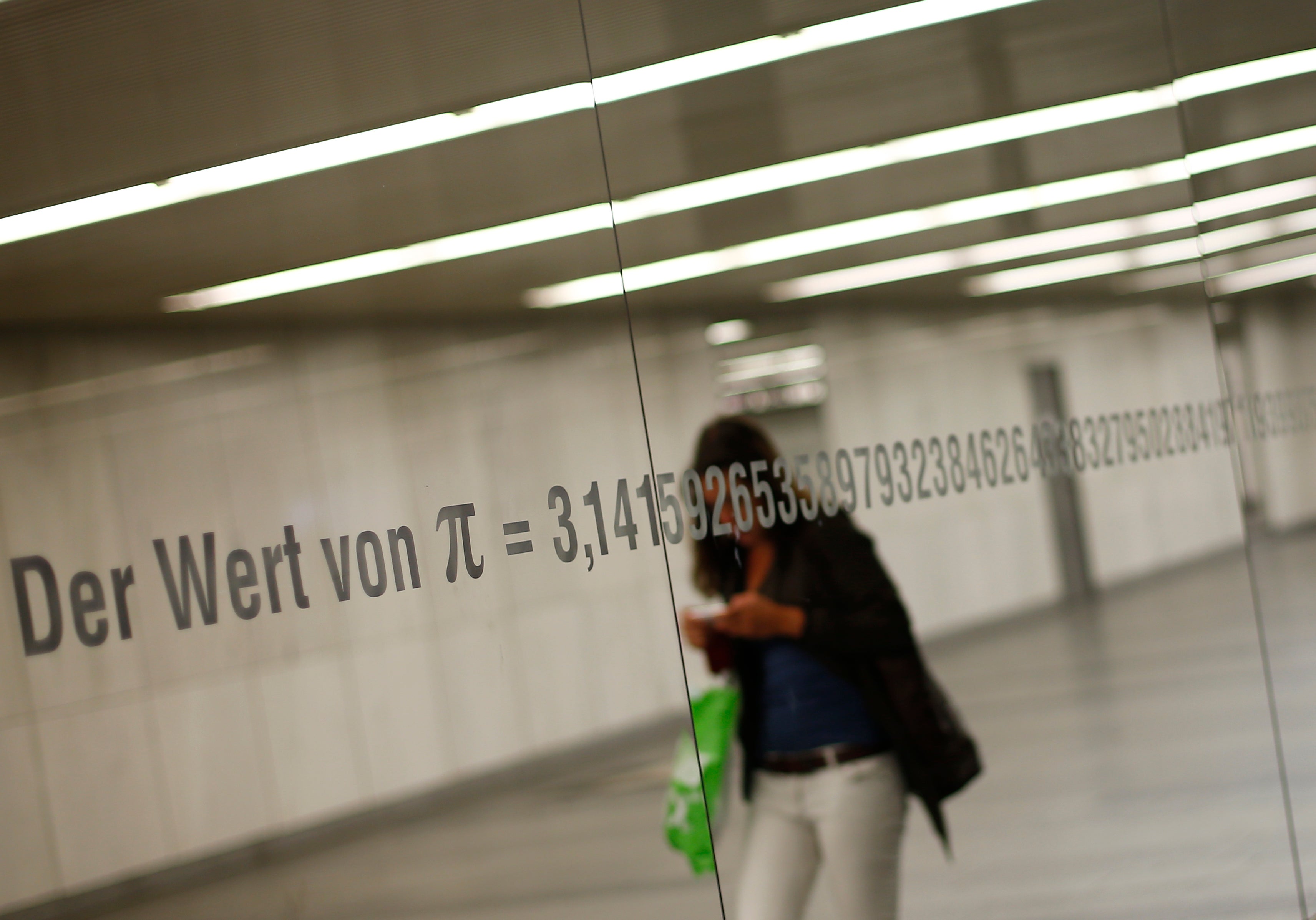 A woman is reflected in a mirror with an inscription reading “The value of Pi” and its numbers in Vienna