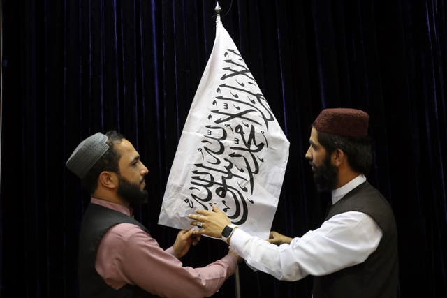 <p>Officials arrange a Taliban flag, before a press conference by spokesman Zabihullah Mujahid</p>