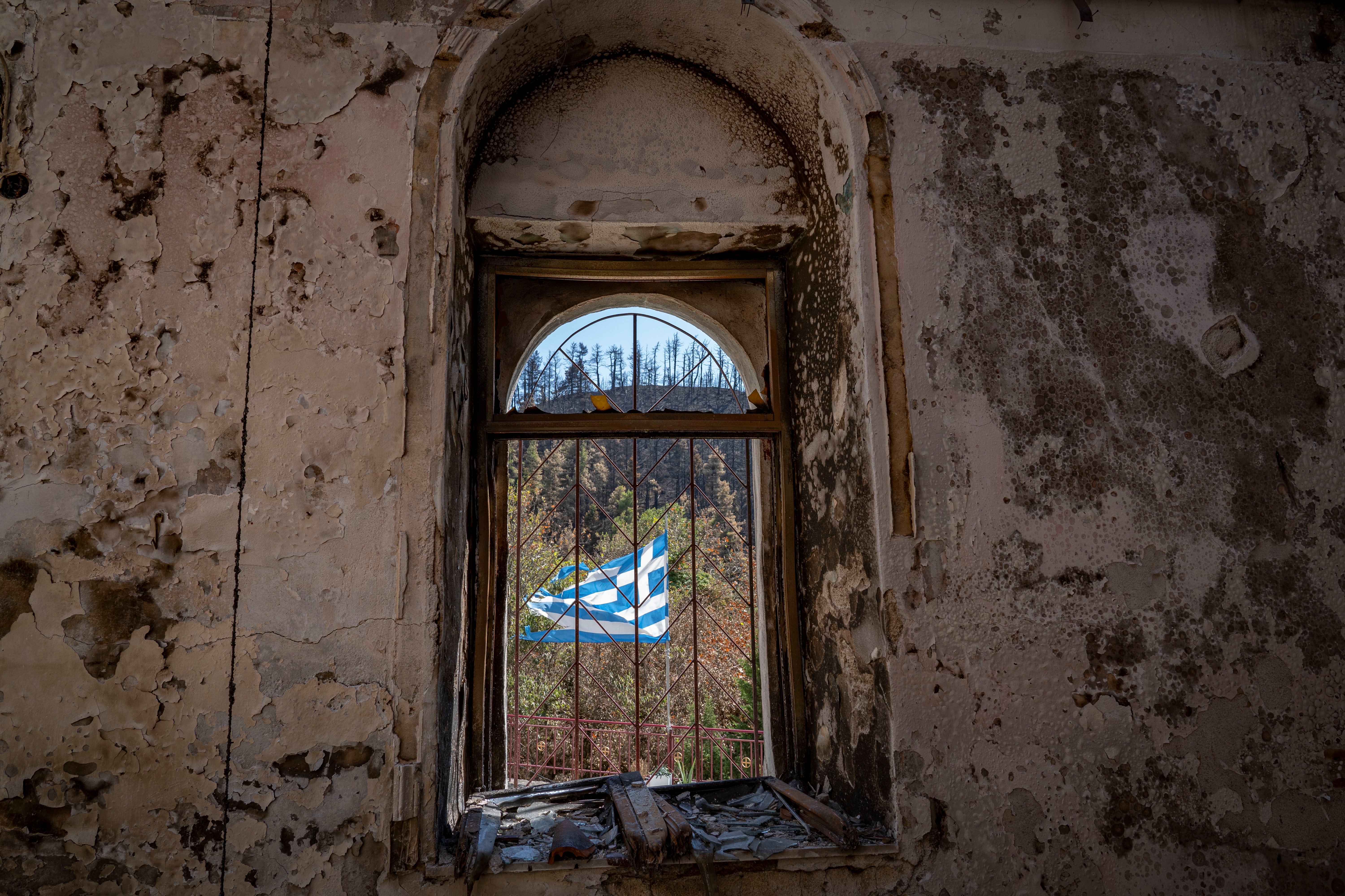 A torn Greek flag seen through the window of a charred house on Evia