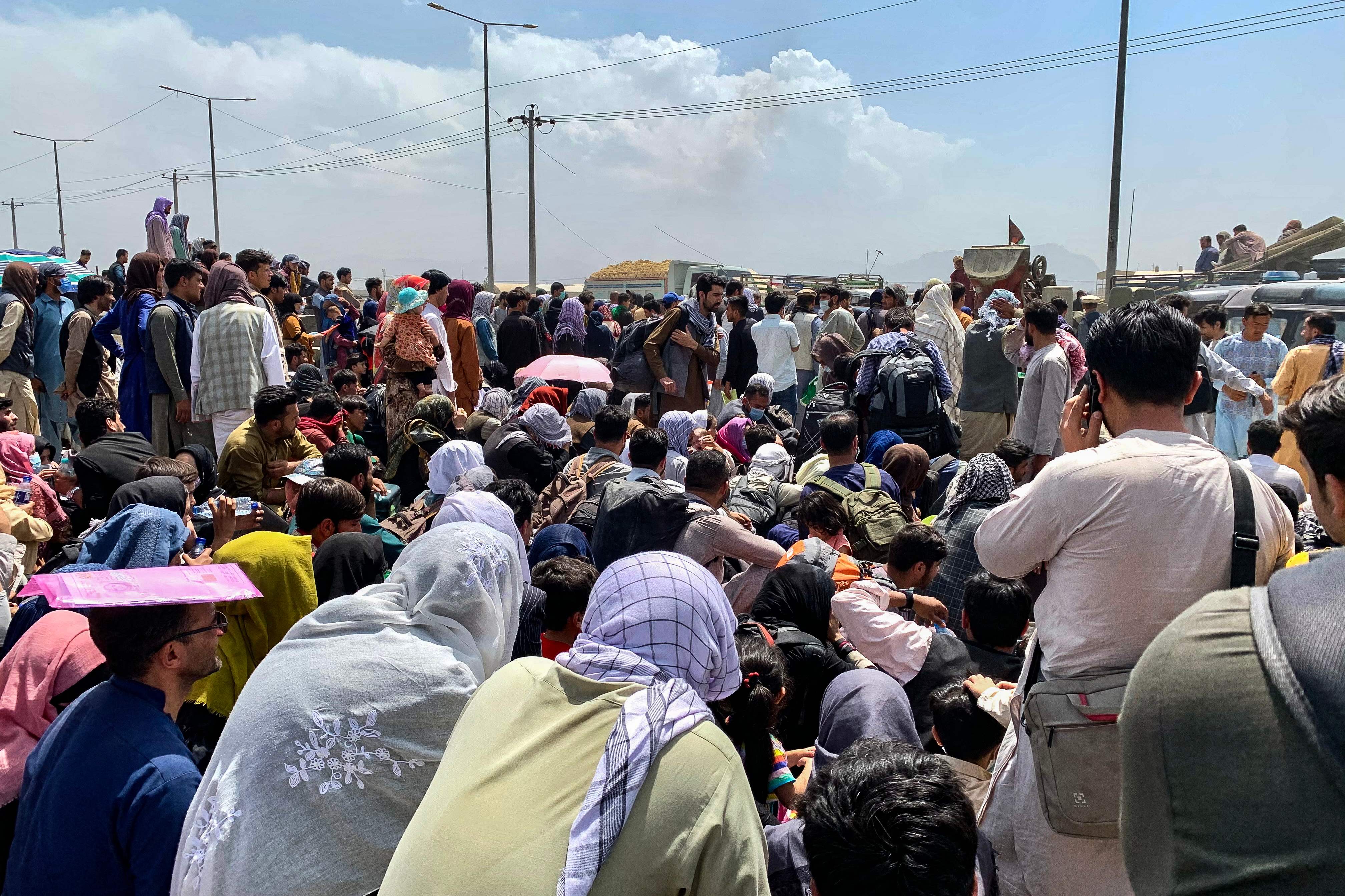 Afghan people gather along a road as they wait to board a US military aircraft to leave the country