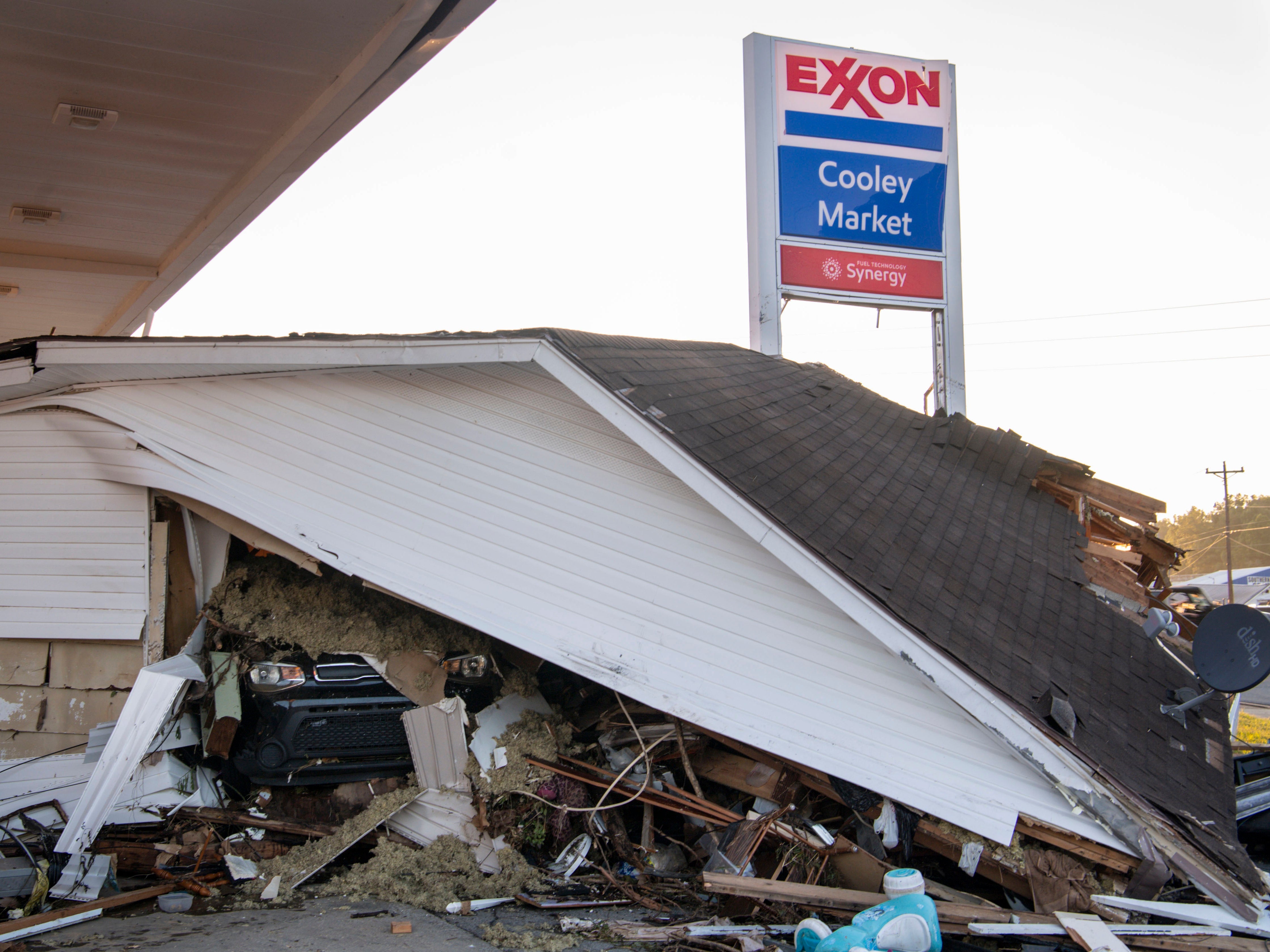 A car peeks out from under a house that was destroyed by floodwaters at the Cooley Market in Waverly, Tennessee