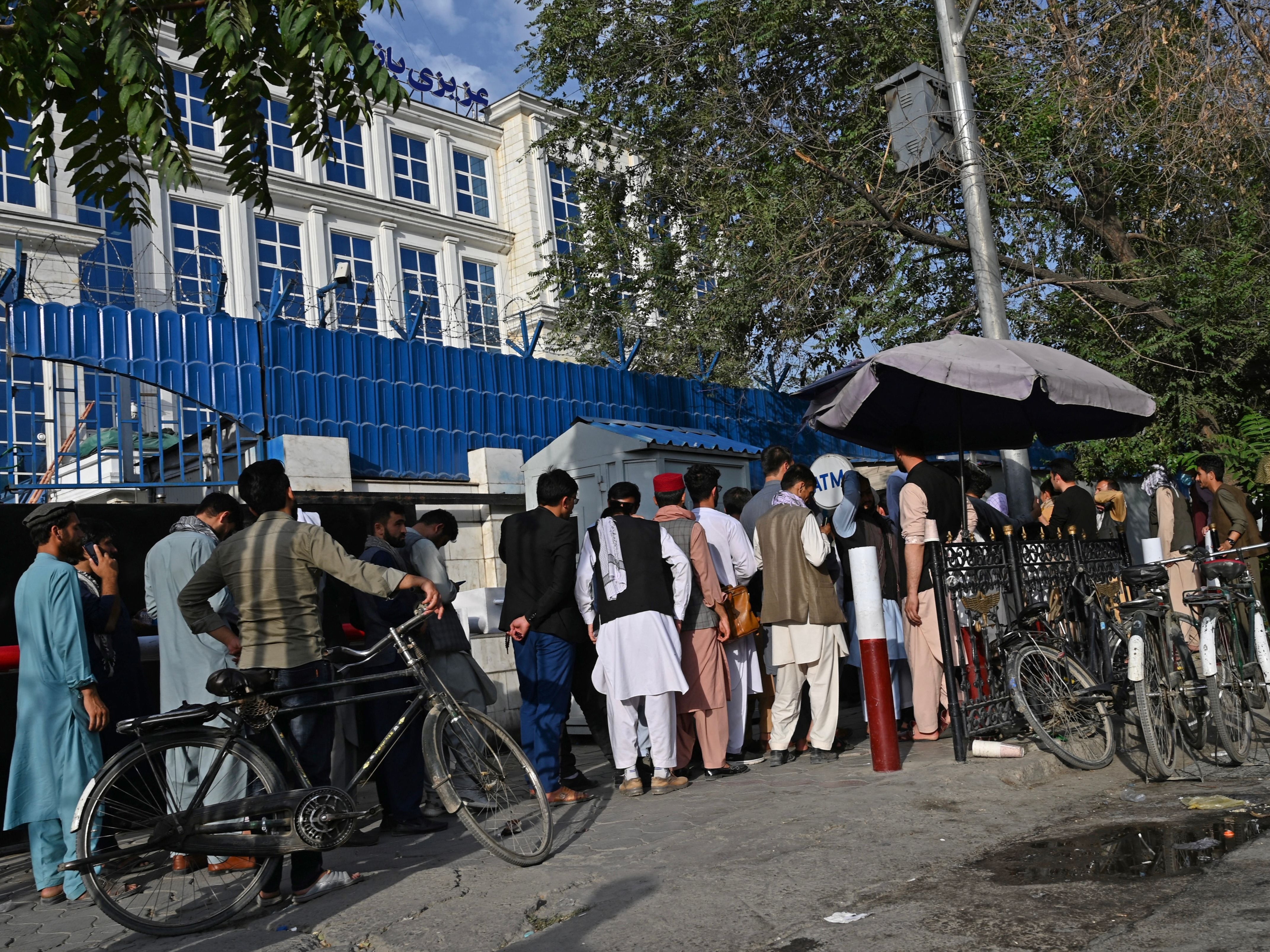 Afghans queue to collect money from an ATM in front of a bank in Kabul after the Taliban takeover