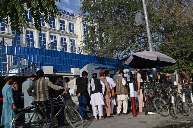 <p>Afghans queue to collect money from an ATM in front of a bank in Kabul after the Taliban takeover</p>