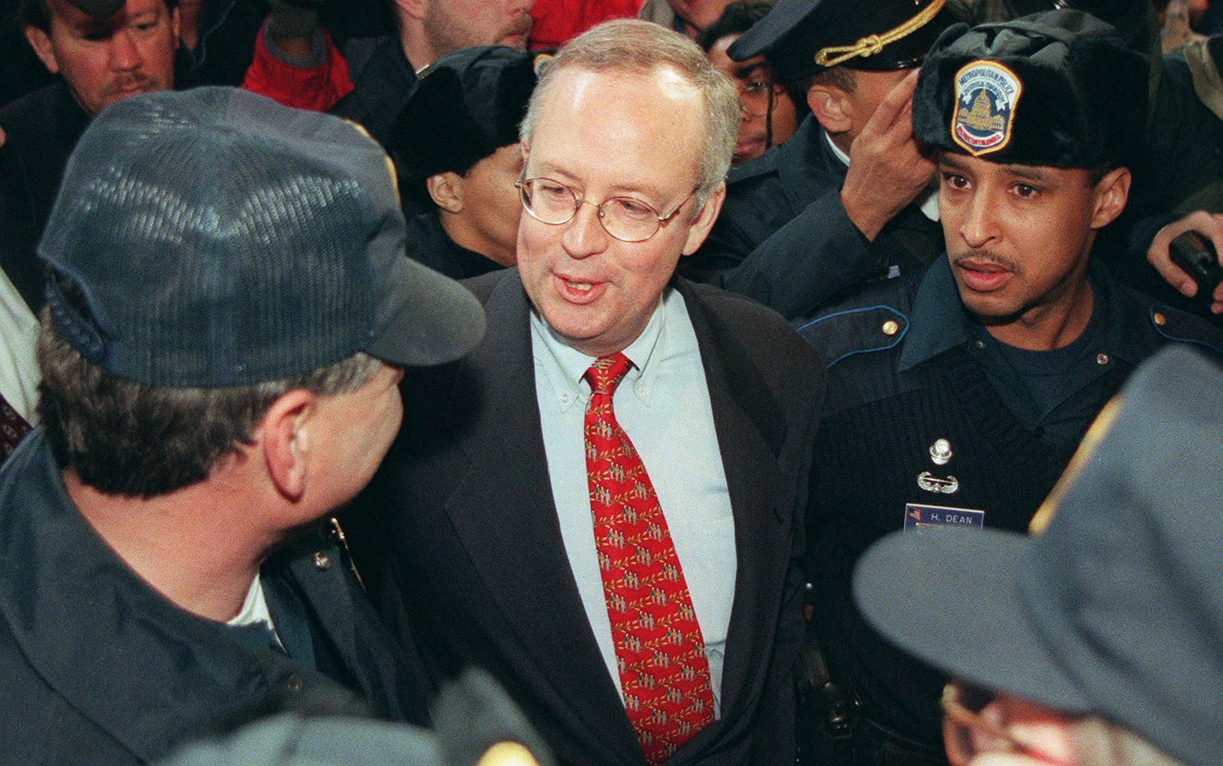 Kenneth Starr, independent counsel, speaks to a Washington, DC police officer as he is escorted away after speaking at a press conference on 22 January 1998