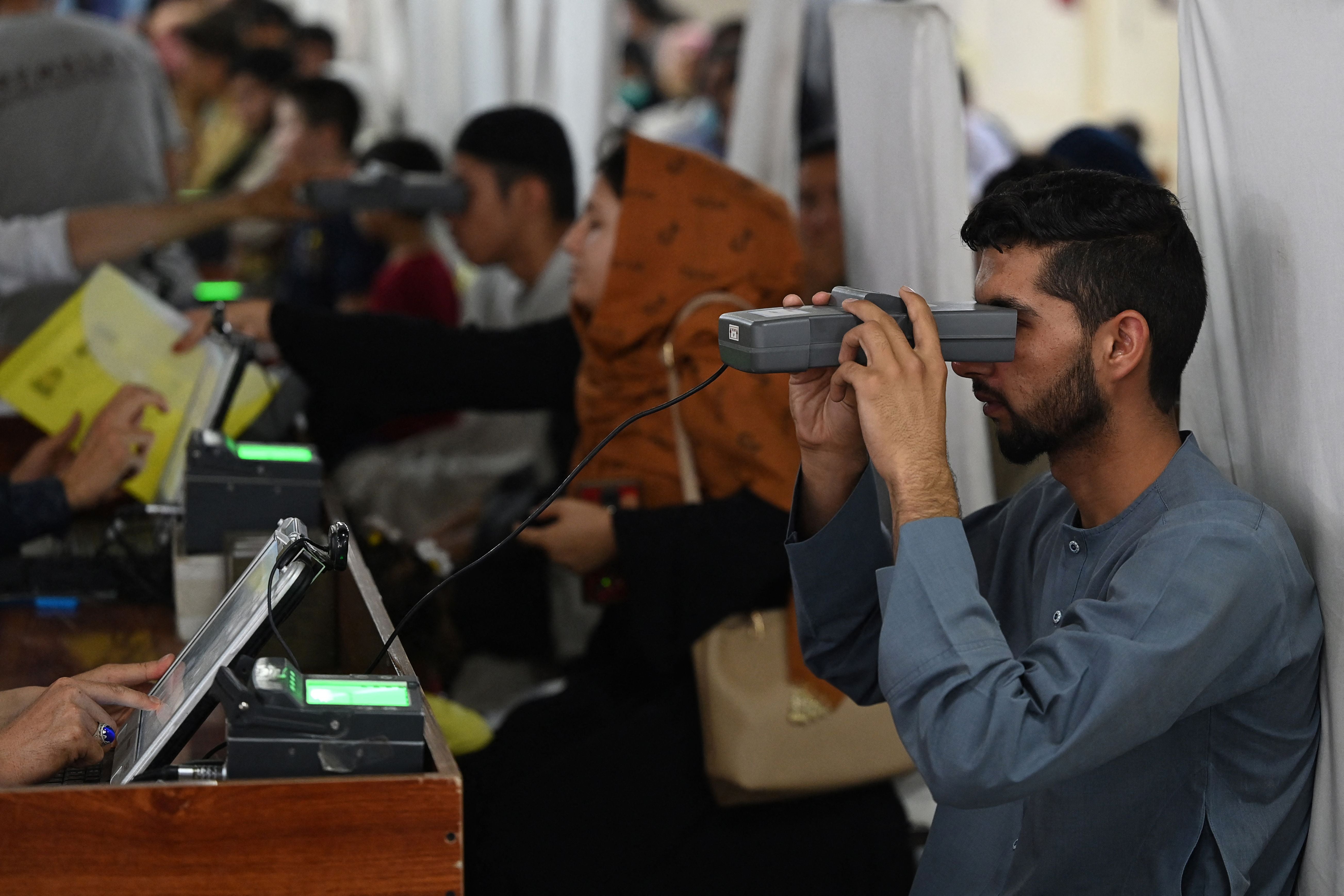 <p>File: A man looks through an optical biometric reader to submit his passport application at an office in Kabul on 25 July 2021</p>