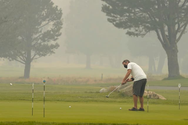 <p>A golfer wears a face mask as he practices his putting at the smoke shrouded Lake Tahoe Golf Course in South Lake Tahoe, Calif., Tuesday, Aug. 24, 2021.</p>