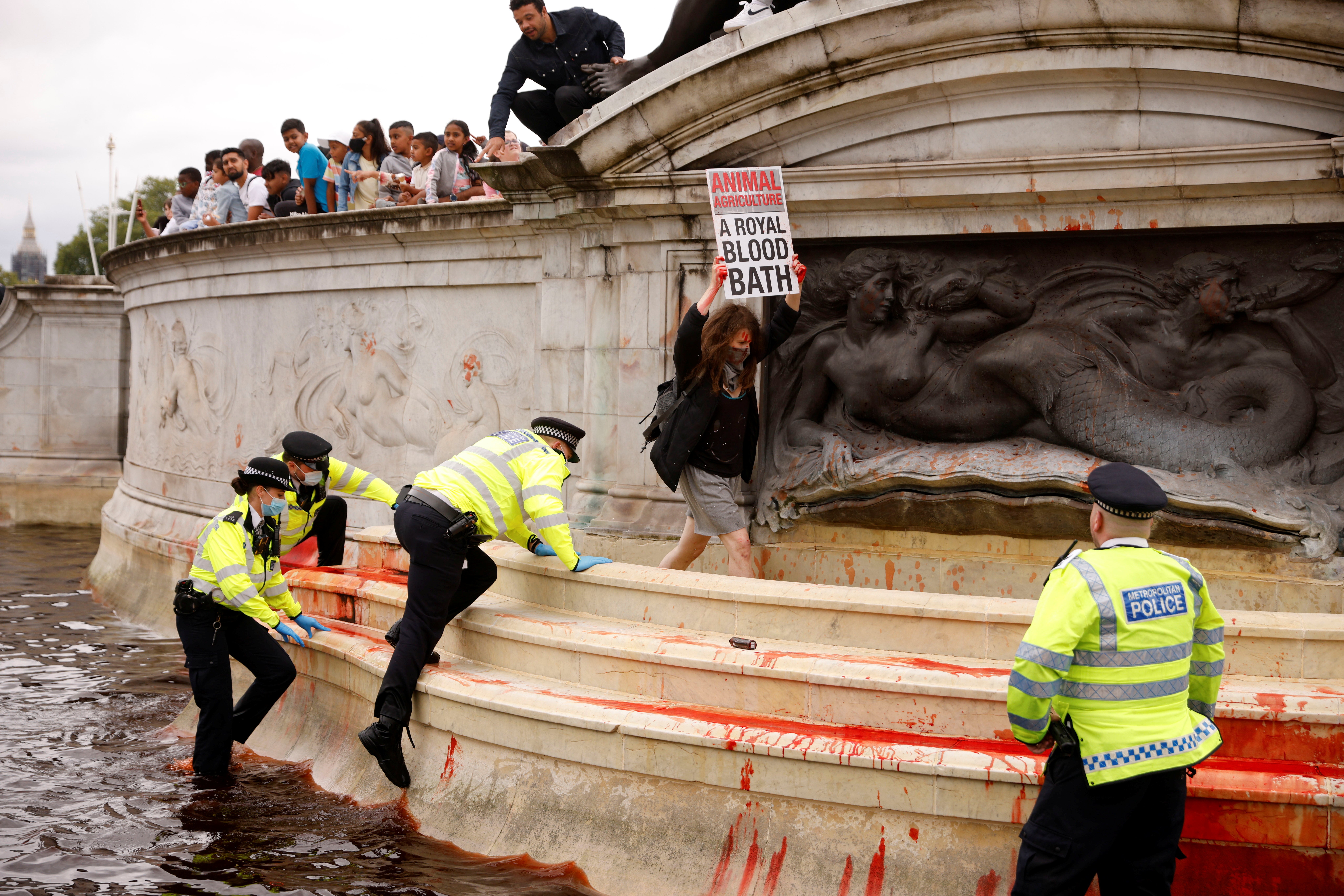 An activist from the organisation Extinction Rebellion holds a poster in a fountain surrounded by police during a protest next to Buckingham Palace in London.