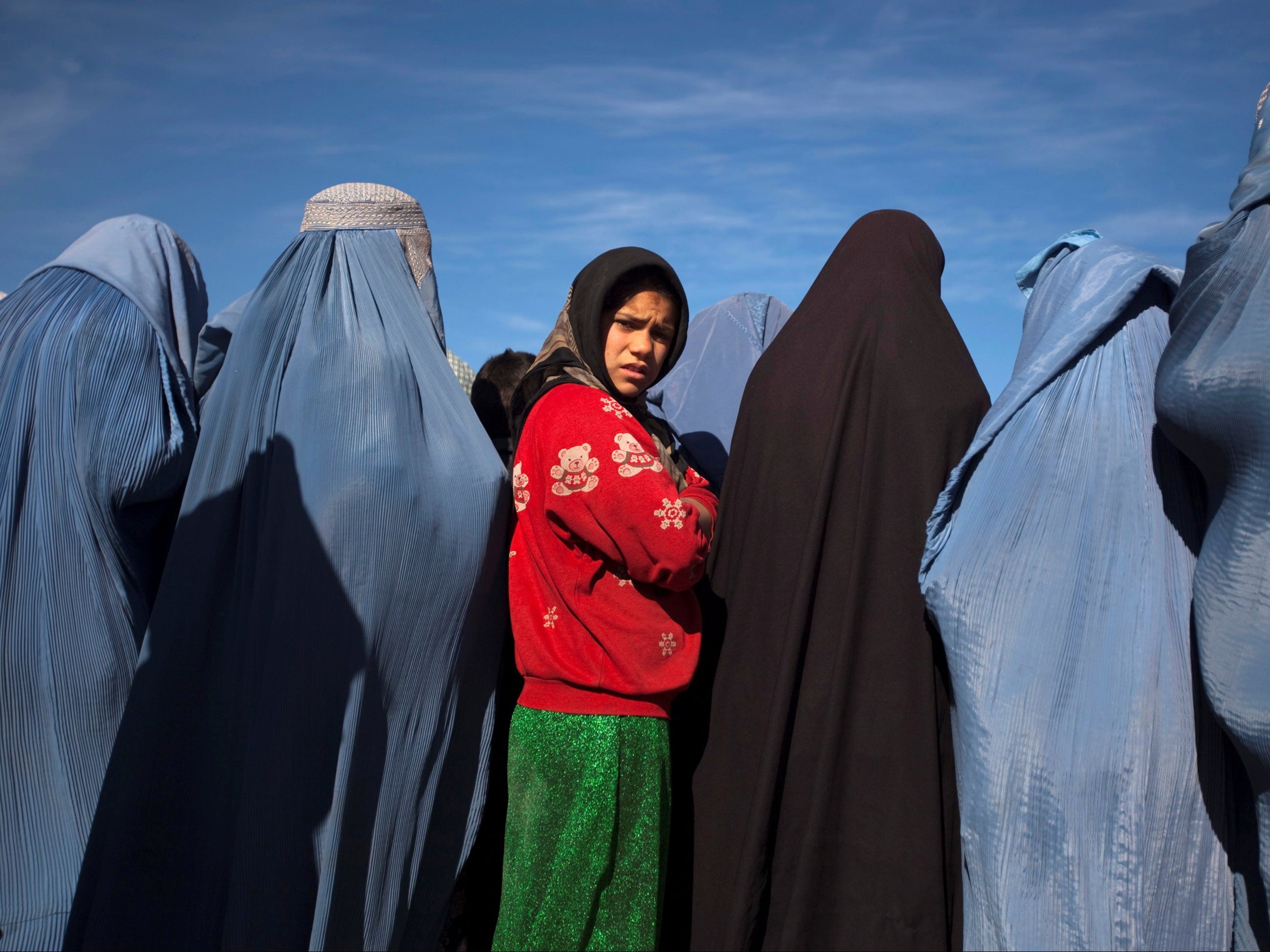An Afghan girl stands among widows clad in burqas