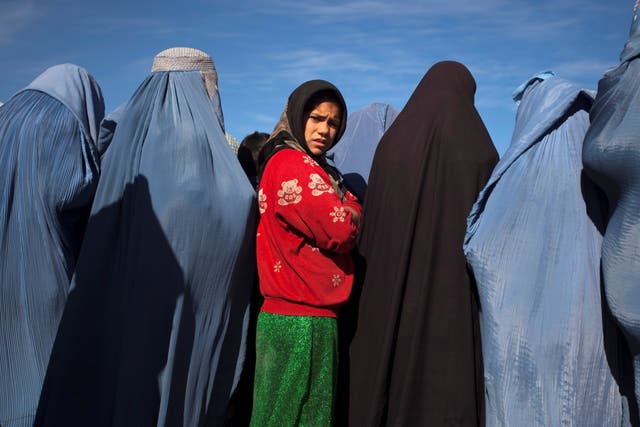 <p>An Afghan girl stands among widows clad in burqas</p>