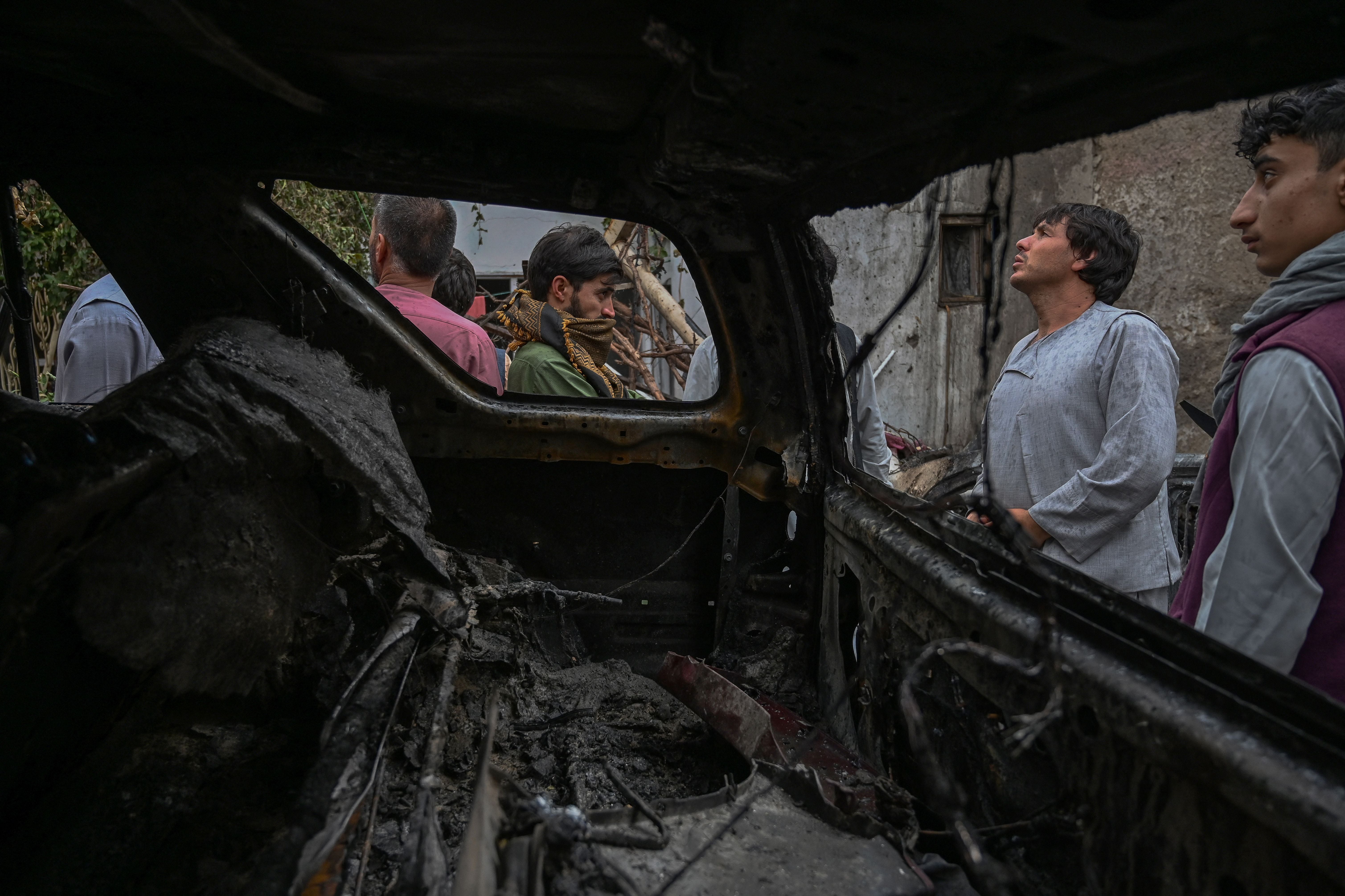 Afghan residents and family members of the victims gather next to a damaged vehicle