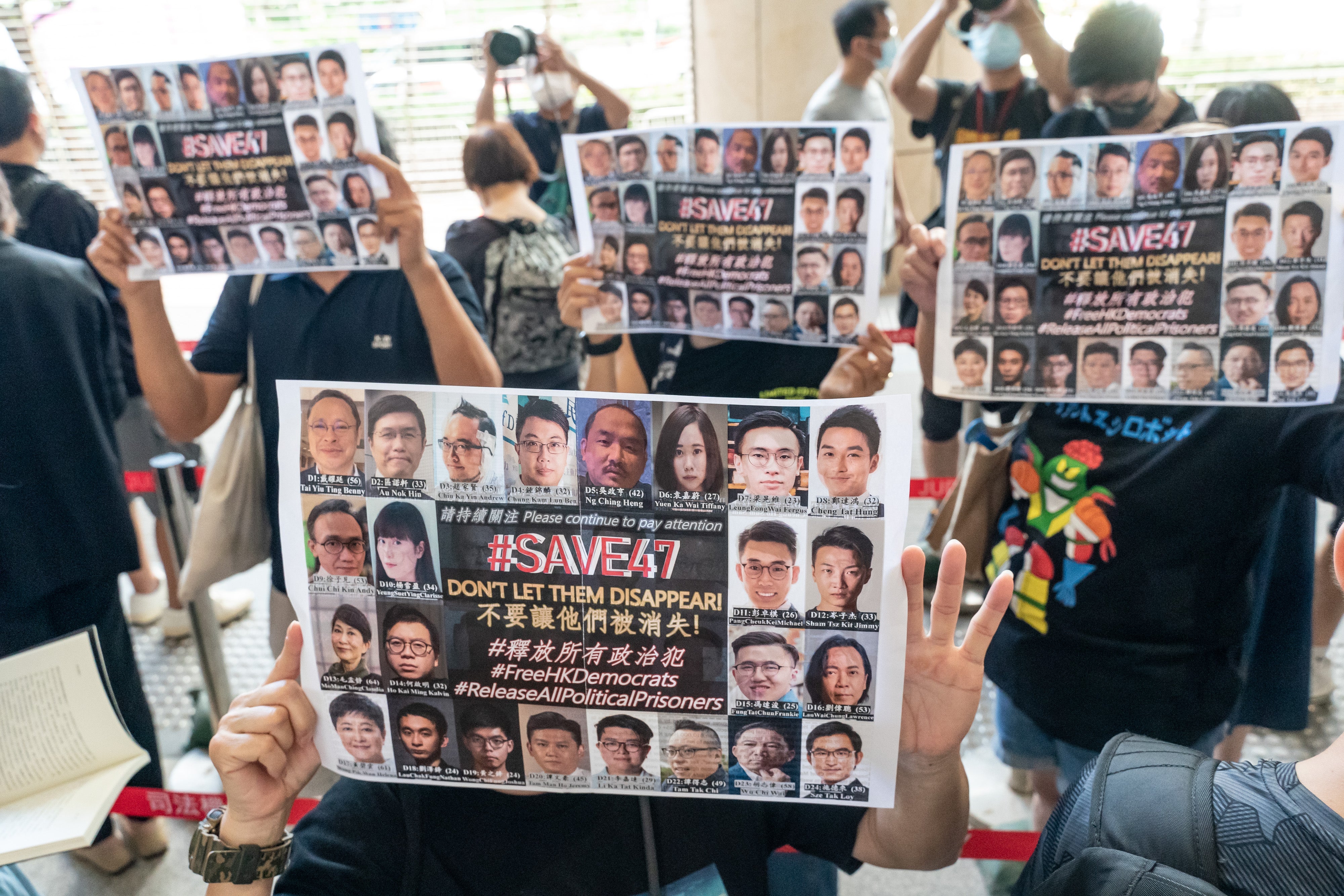 Supporters hold signs featuring images of some of the 47 pro-democracy activists outside the West Kowloon Magistrates' Courts ahead of a hearing