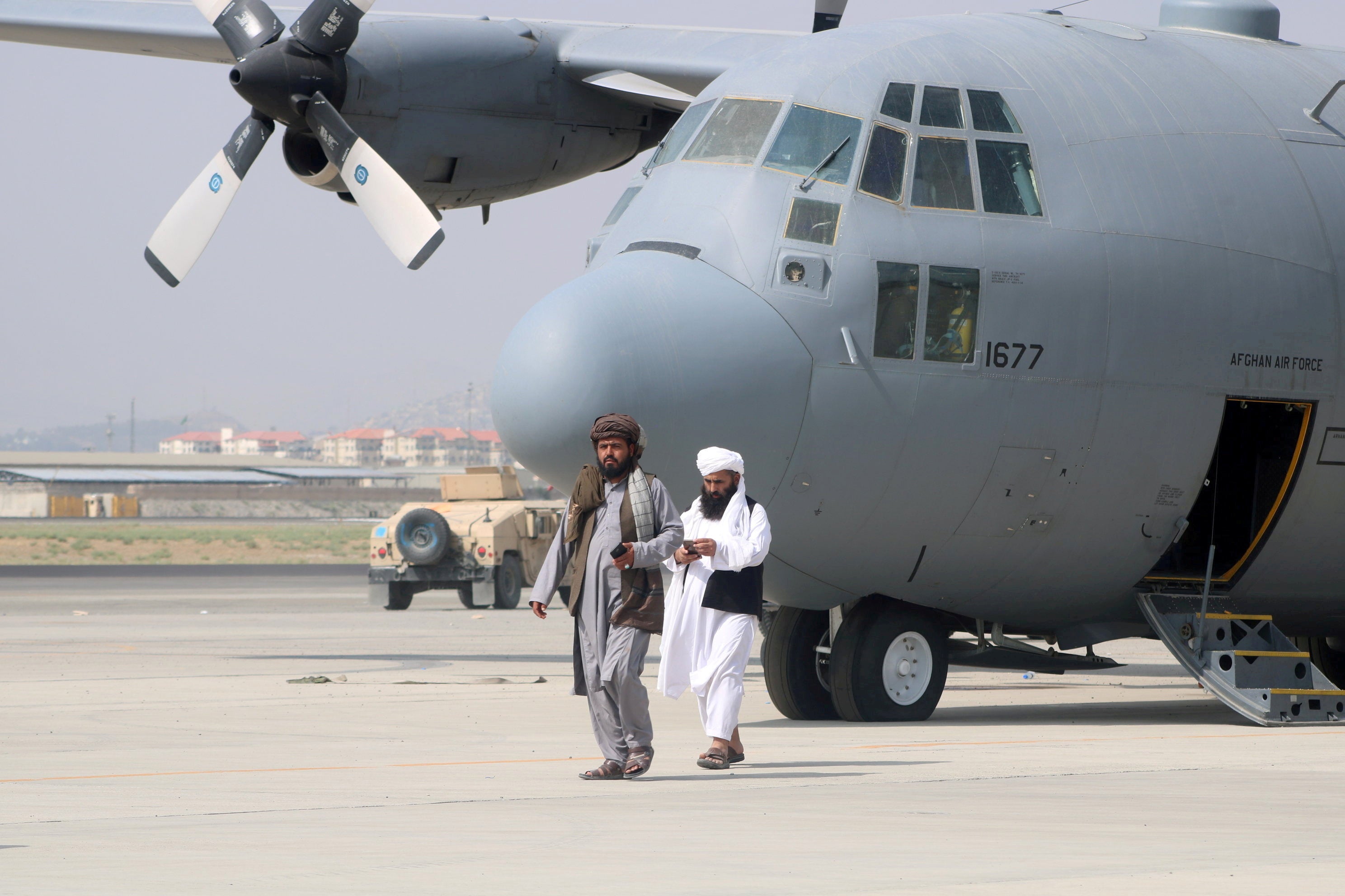 Taliban fighters walk in front of a military plane on Tuesday after sweeping the country in a matter of weeks
